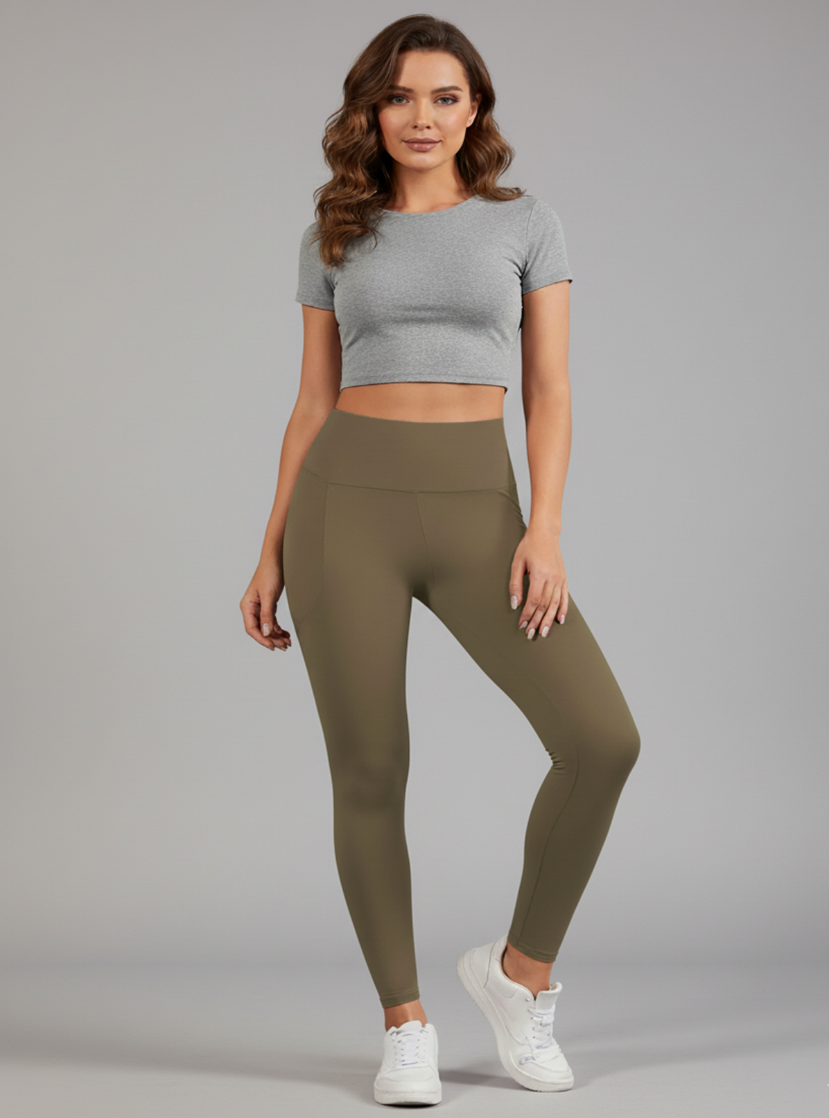 Woman wearing a gray crop top and olive green leggings on a gray background