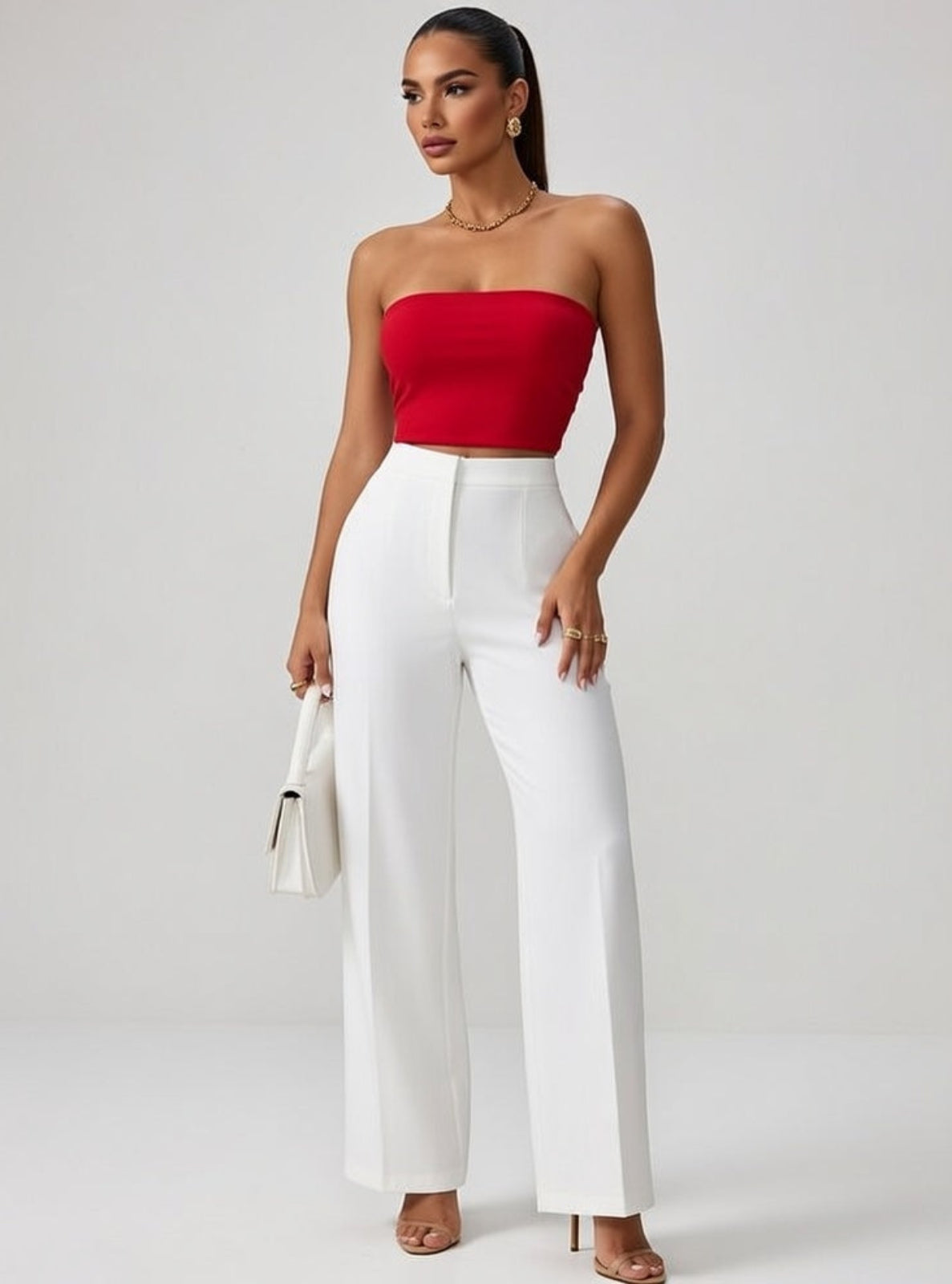 Woman wearing a red strapless top and white pants against a gray background