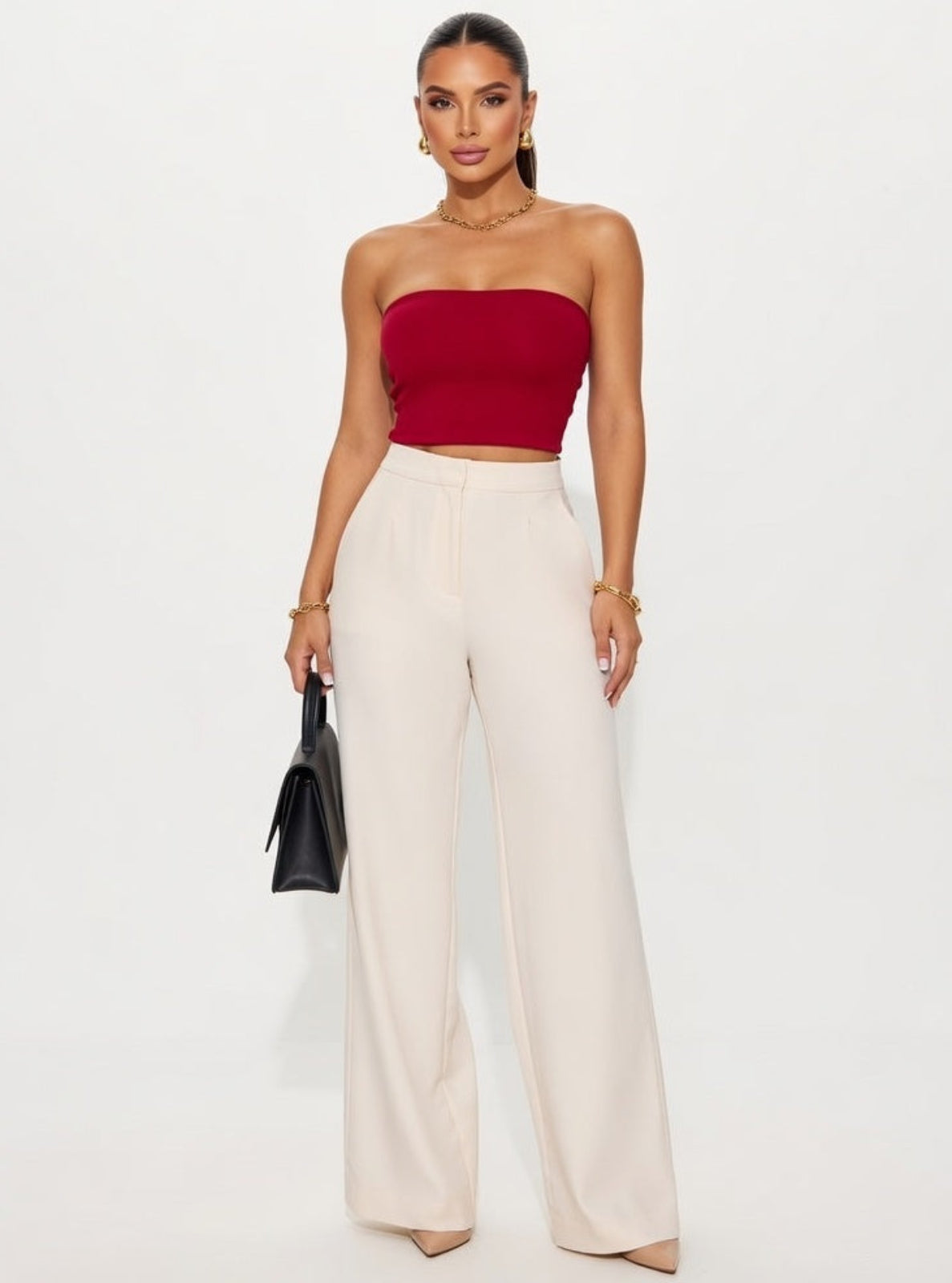 Woman wearing a red strapless top and white pants on a plain background