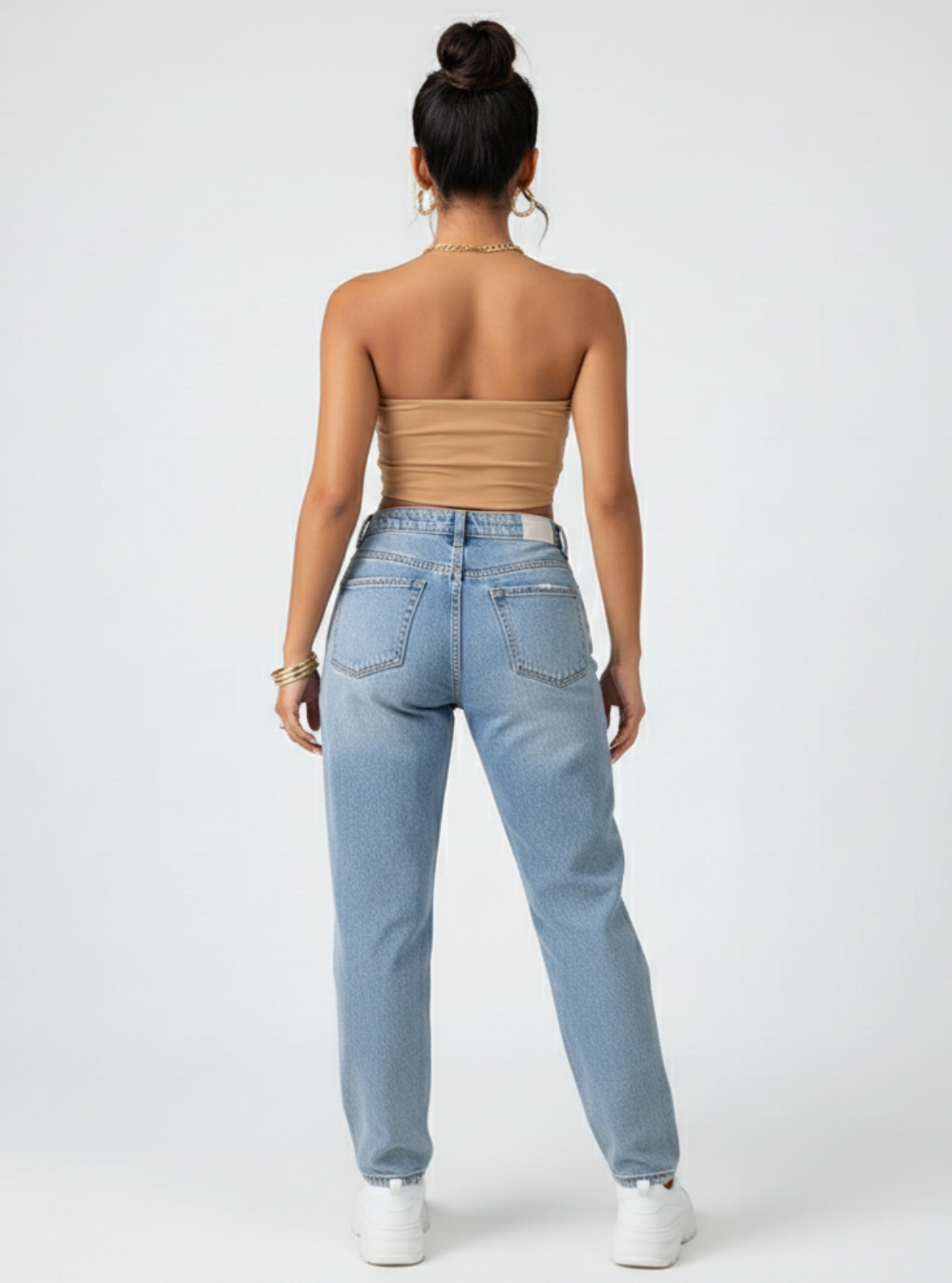 Woman wearing light blue jeans and a beige strapless top on a white background