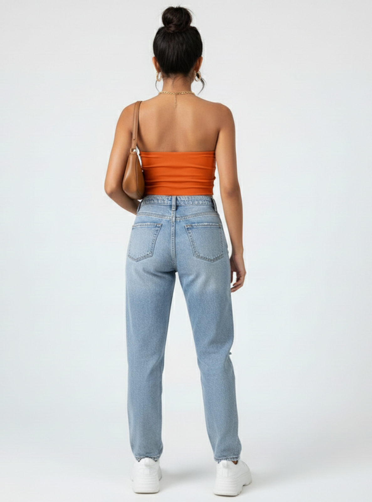 Woman wearing an orange strapless top and light blue jeans on a white background
