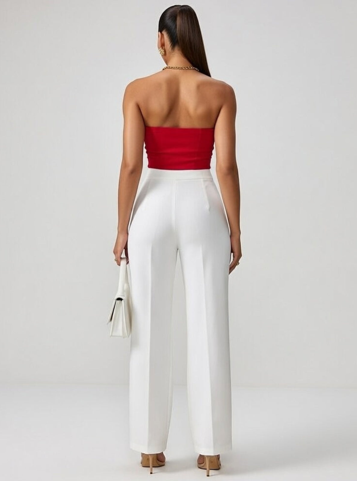 Woman wearing a red strapless top and white pants on a plain background