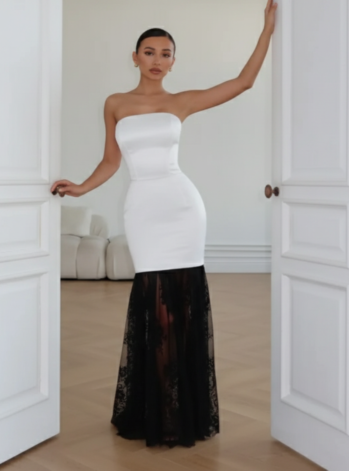 Woman in a strapless white dress with a black bottom half standing in a doorway.
