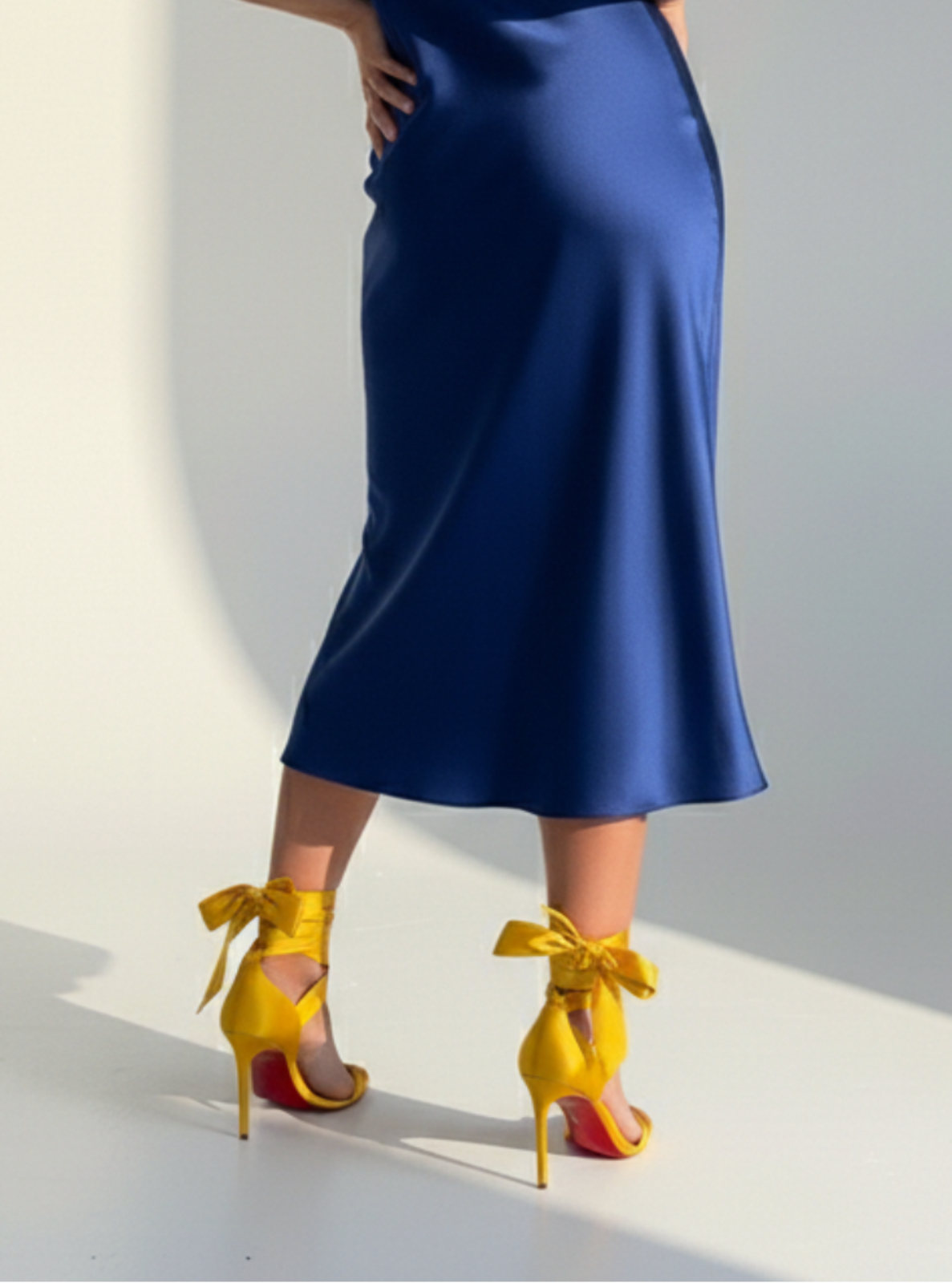Woman in a blue satin dress with yellow heels standing against a gray background