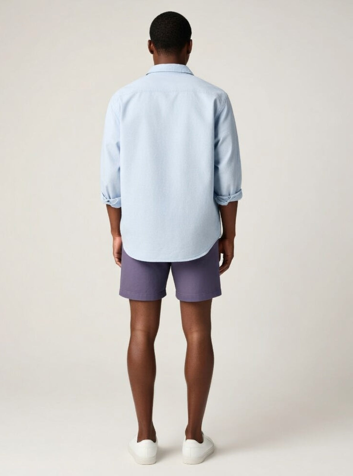 Man wearing a light blue shirt and purple shorts on a plain background