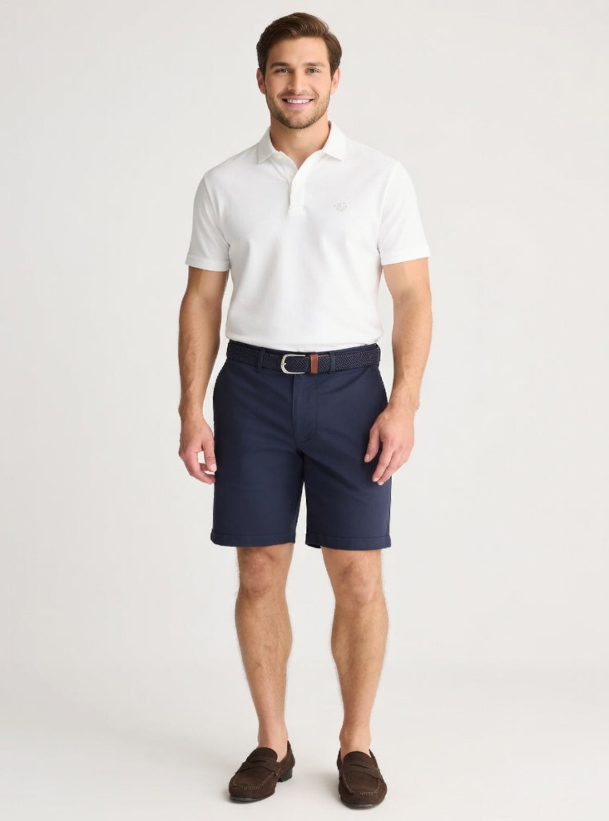 Man wearing a white polo shirt and navy shorts on a light gray background