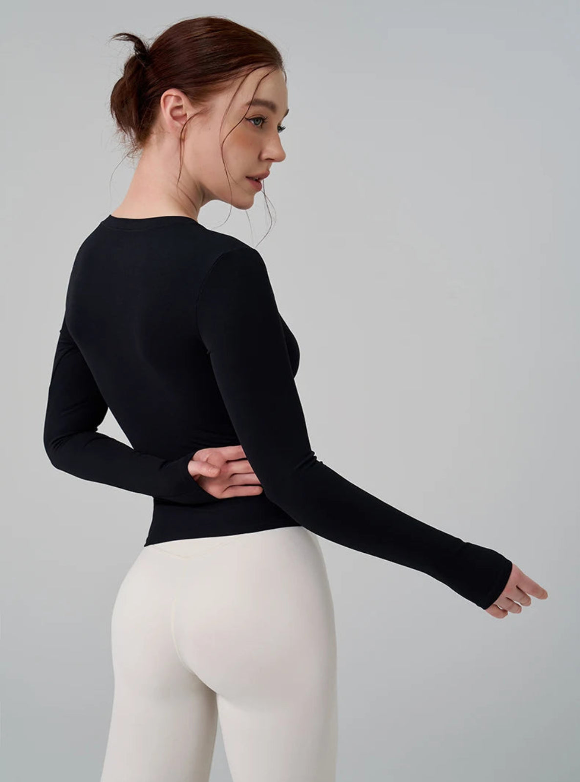 Woman wearing a black long-sleeve top and white leggings on a gray background