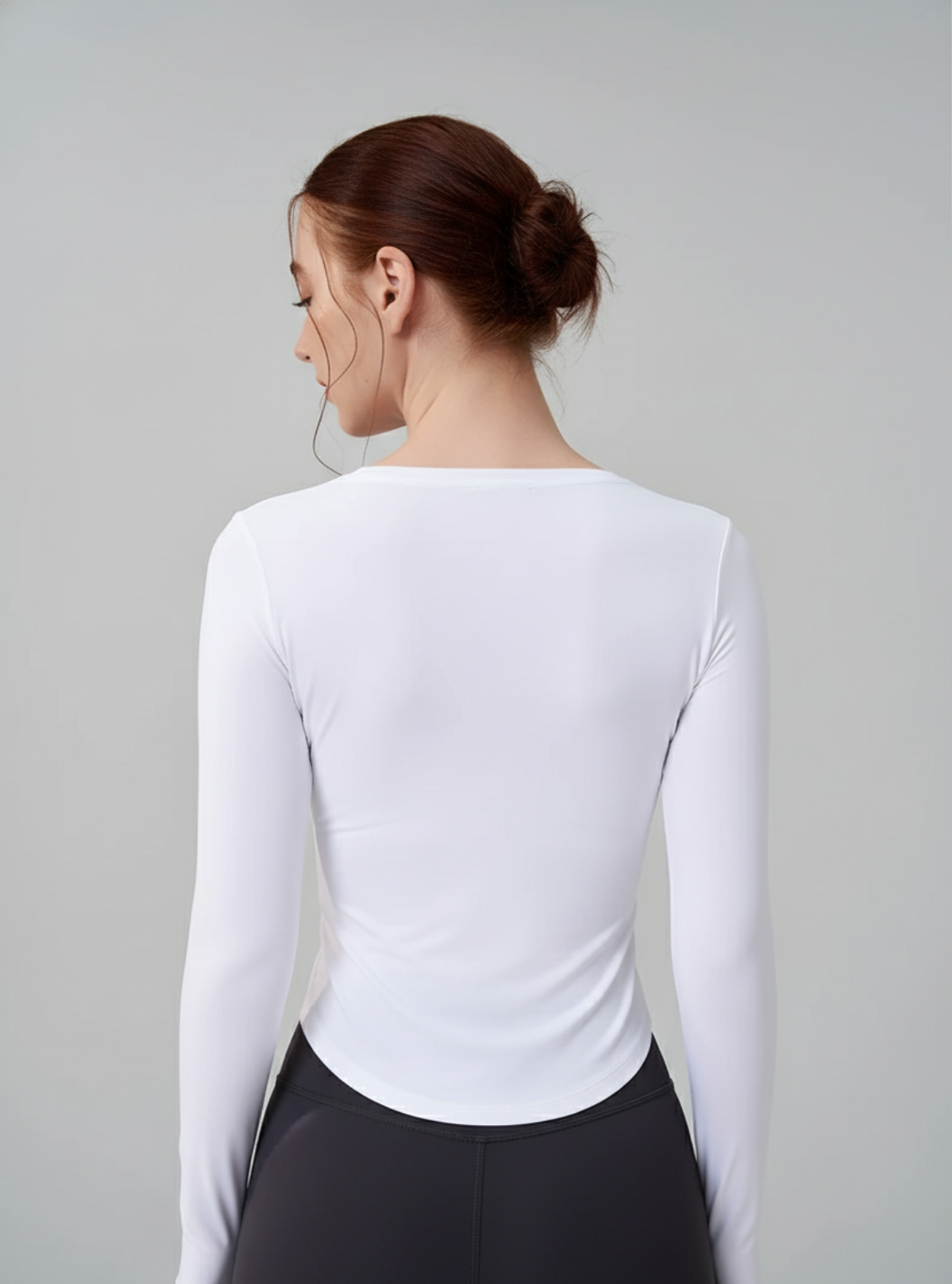 Woman wearing a white long-sleeve top and black leggings against a gray background