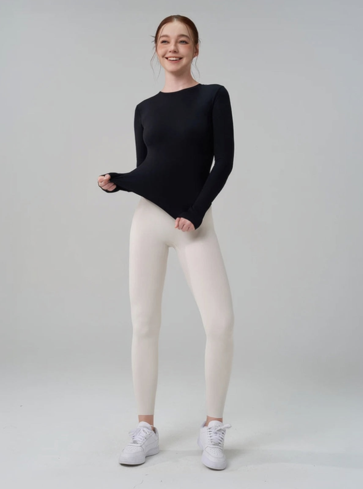 Person wearing a black long-sleeve top and white leggings on a plain background