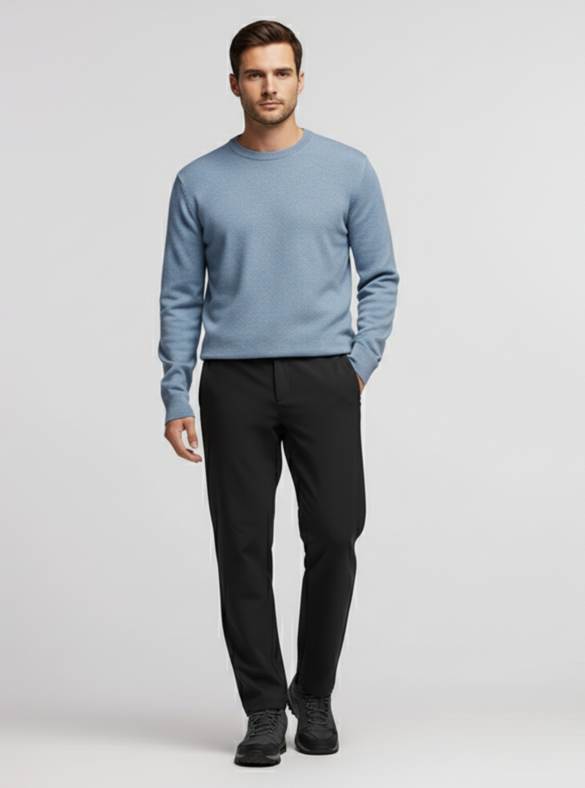 Man wearing a light blue sweater and black pants on a plain background