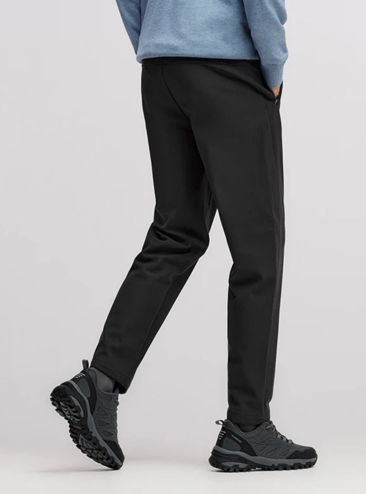 Person wearing black pants and black shoes on a light gray background