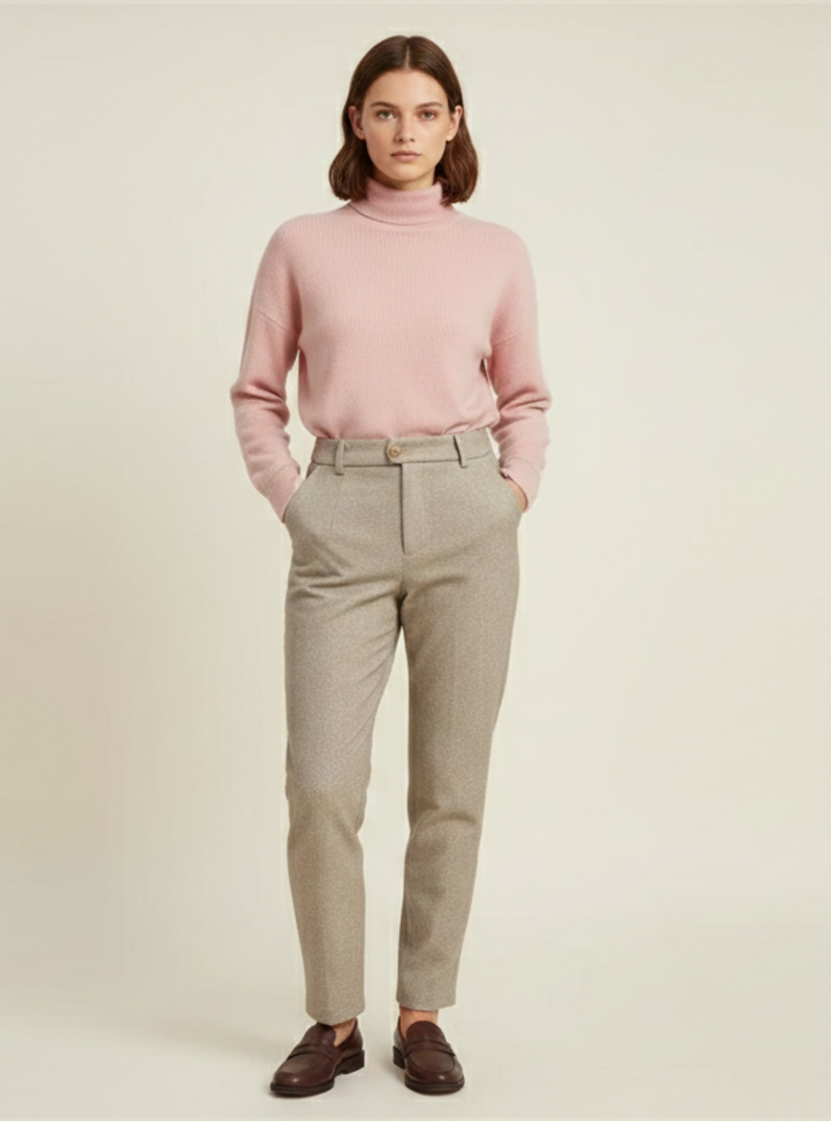 Woman wearing a pink sweater and beige pants on a plain background
