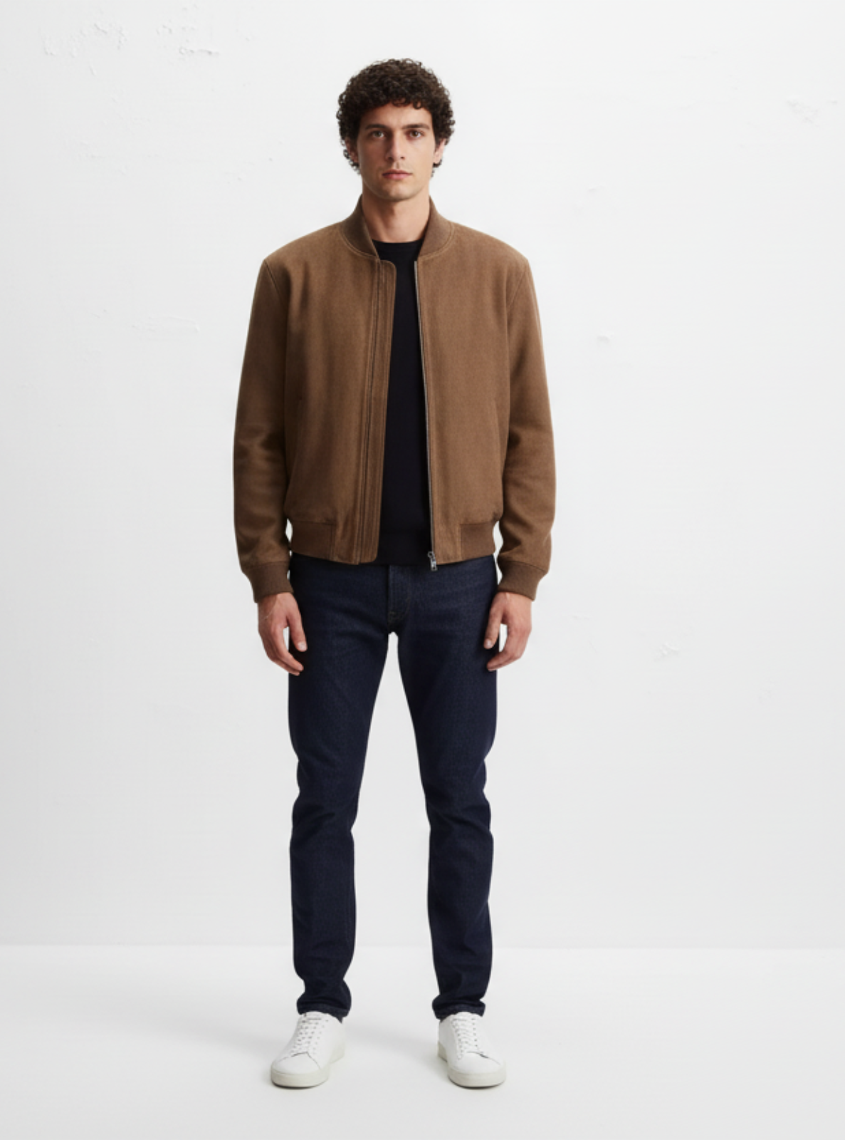 Man wearing a brown jacket and dark jeans on a white background