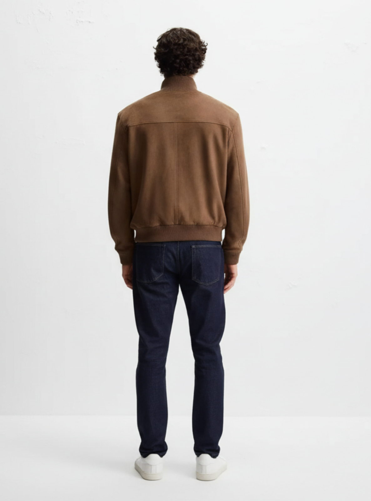 Man wearing a brown jacket and dark jeans on a white background