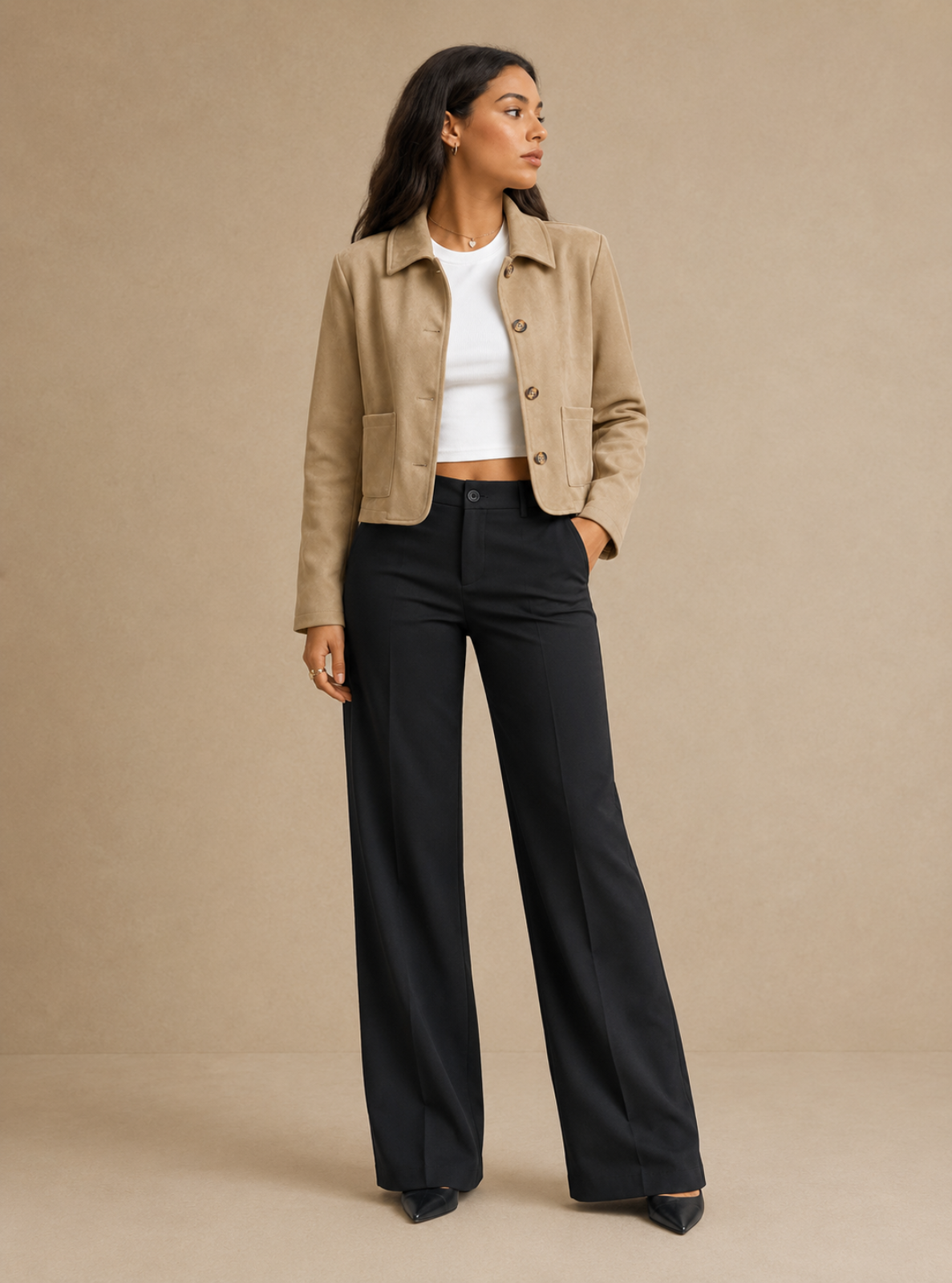 A woman models a beige cropped suede jacket, a white ribbed crop top, and black wide-leg trousers against a solid beige studio backdrop.