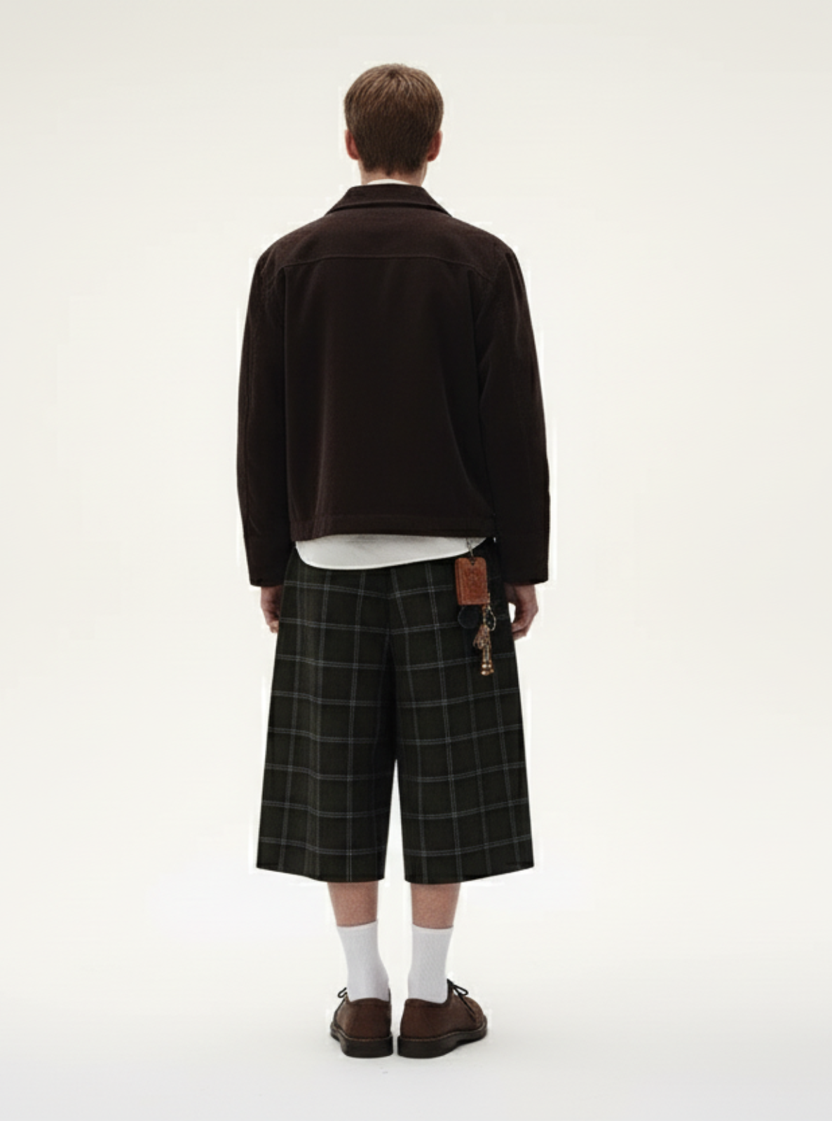 Person wearing a dark jacket, plaid skirt, and white socks on a white background