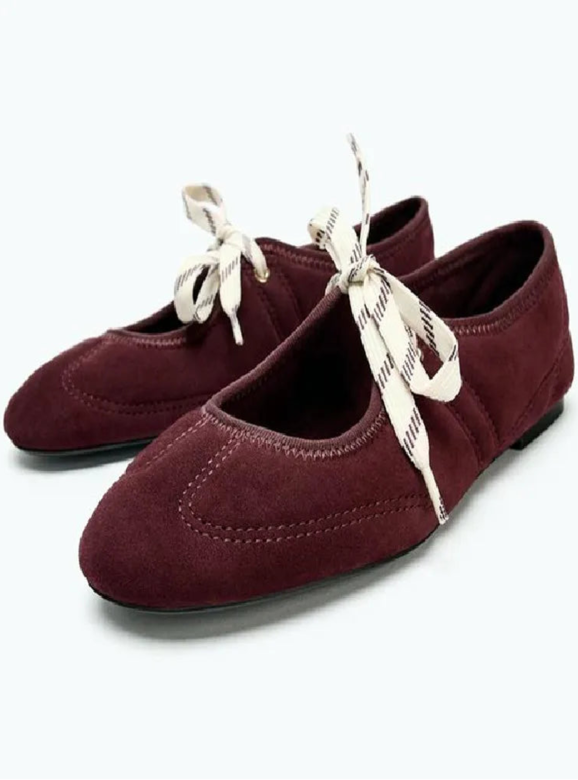 Pair of maroon ballet flats with white laces on a white background