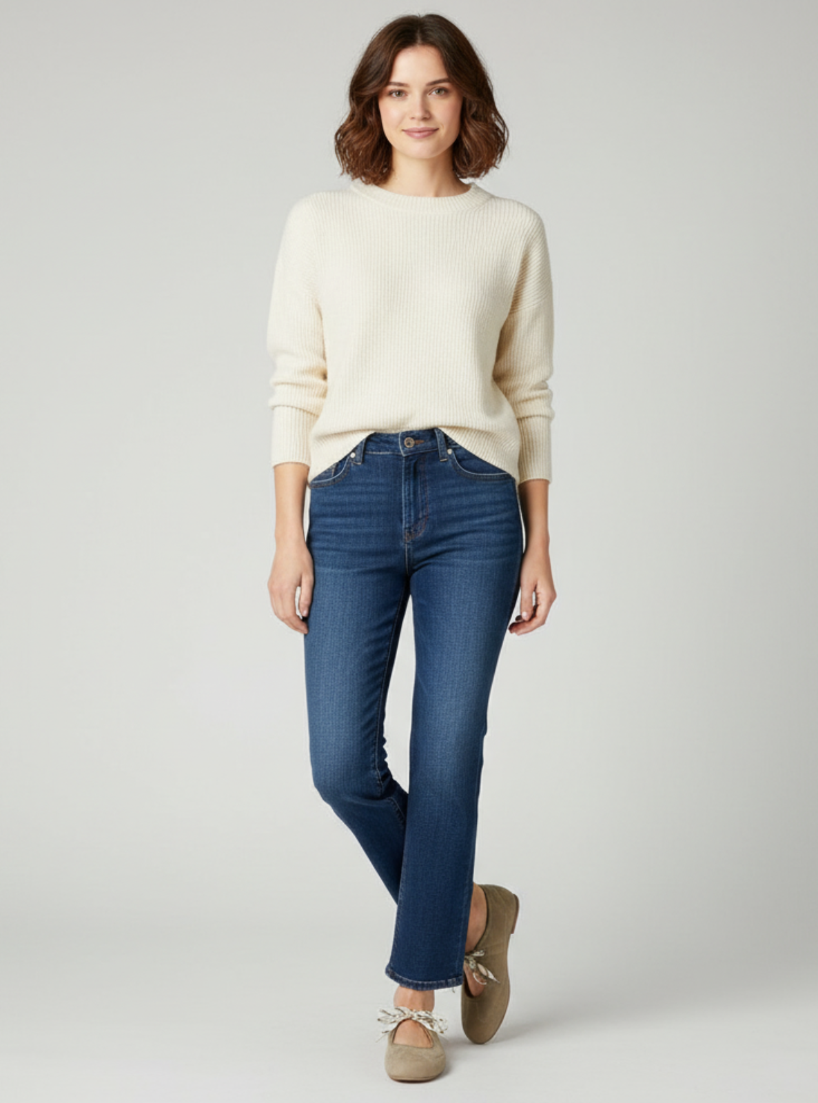 Woman wearing a cream sweater and blue jeans on a gray background