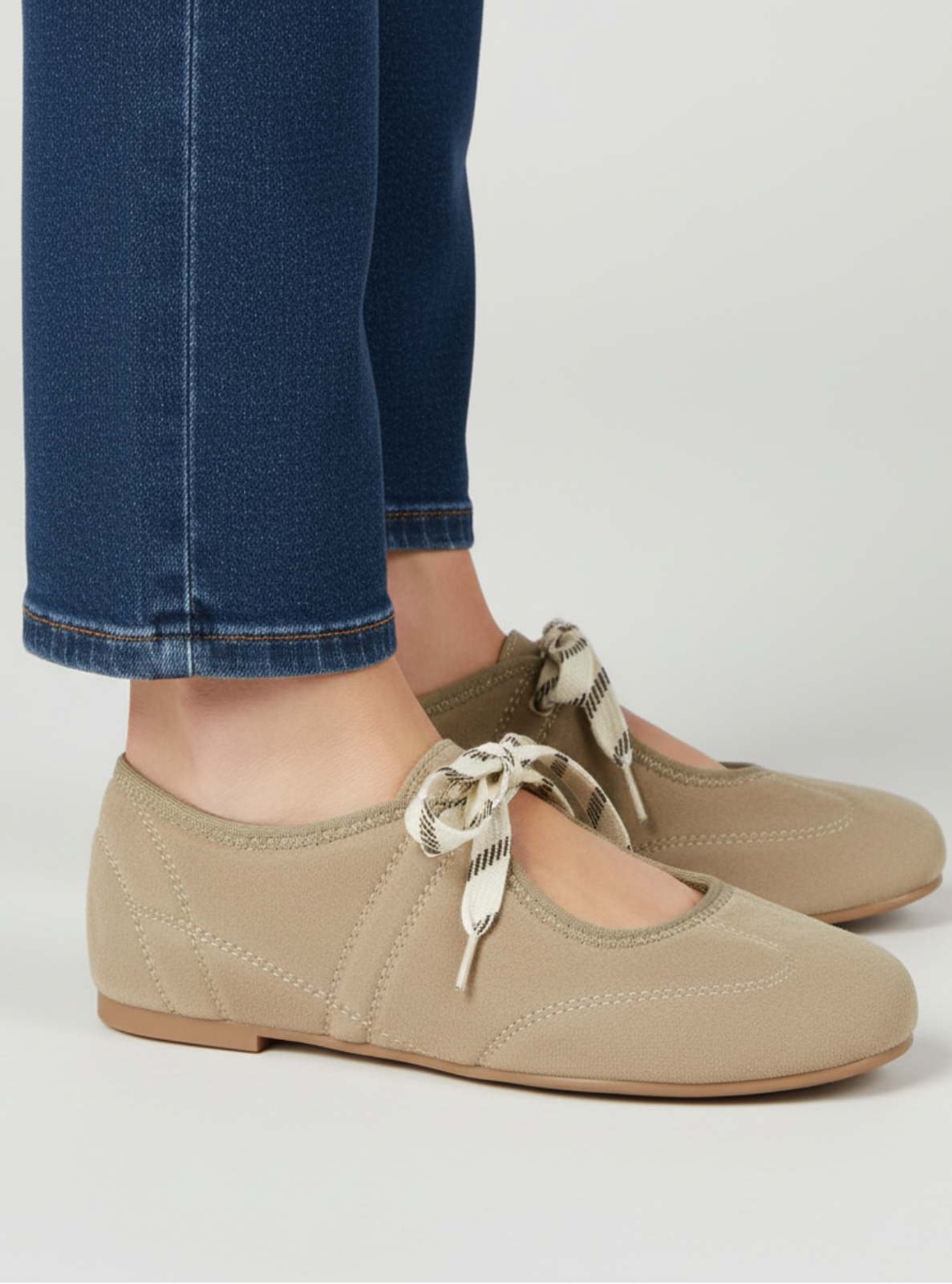 Beige shoes with bow details worn with blue jeans on a light gray background