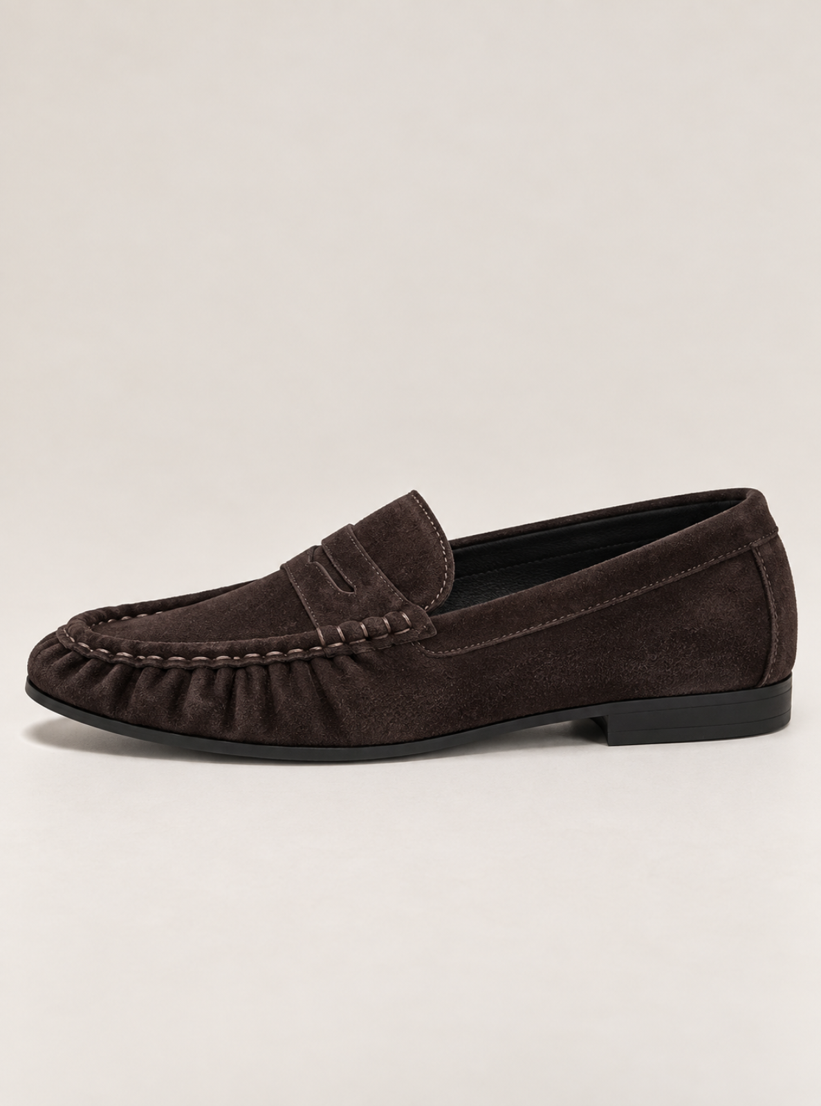 A dark brown suede penny loafer shown from a side profile view against a light beige studio background.