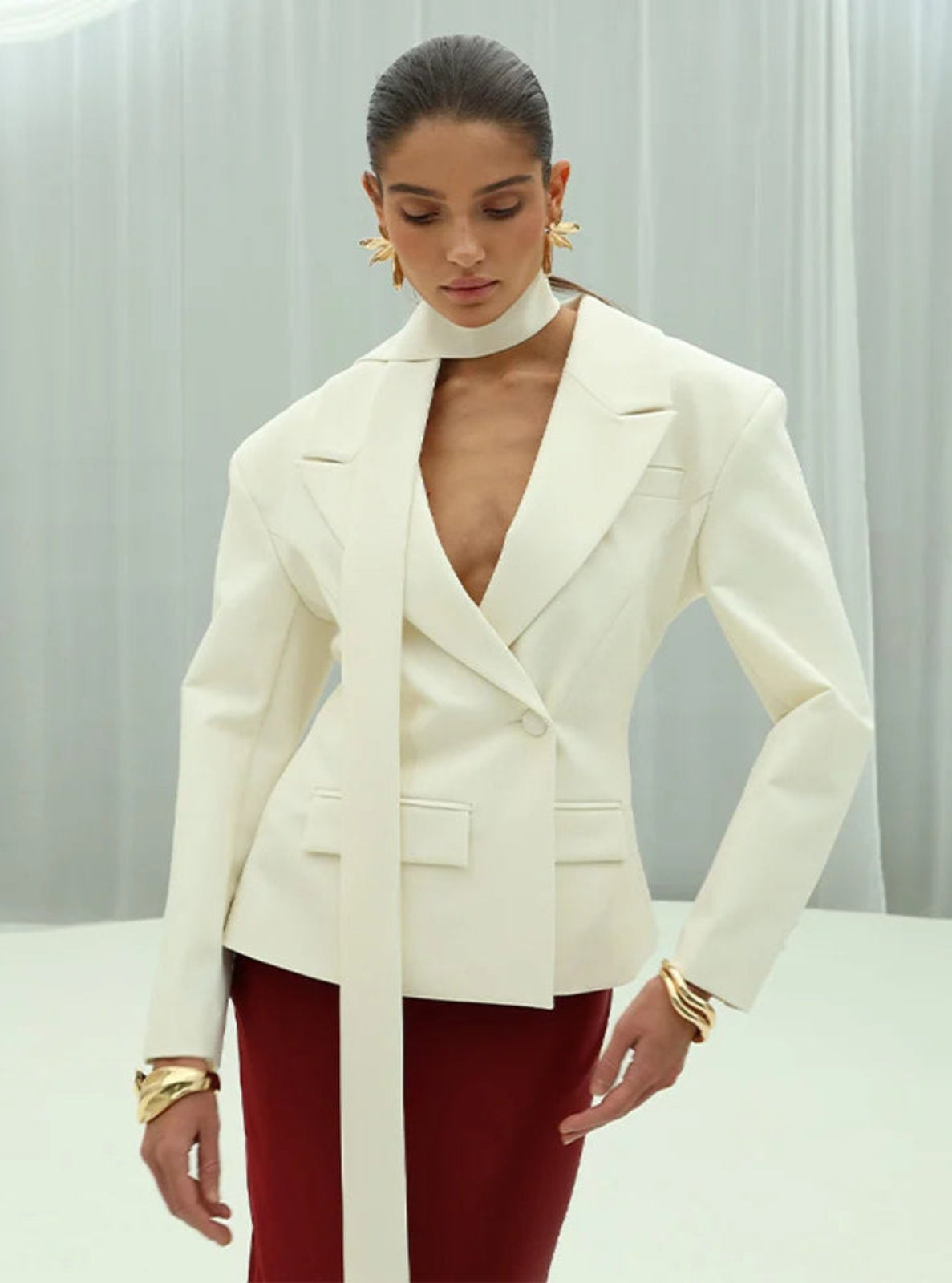 Woman wearing a white blazer over a red outfit with gold jewelry against a light gray background
