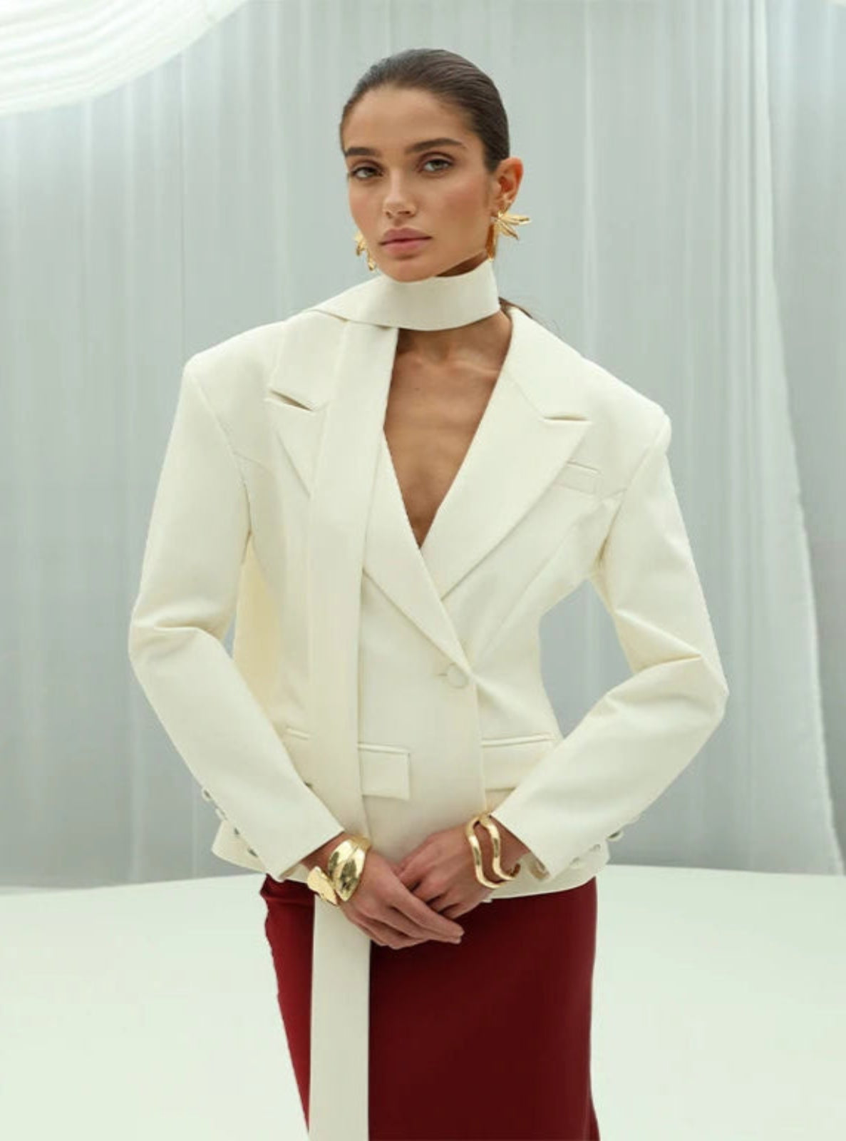Woman wearing a white blazer over a red dress with a plain background