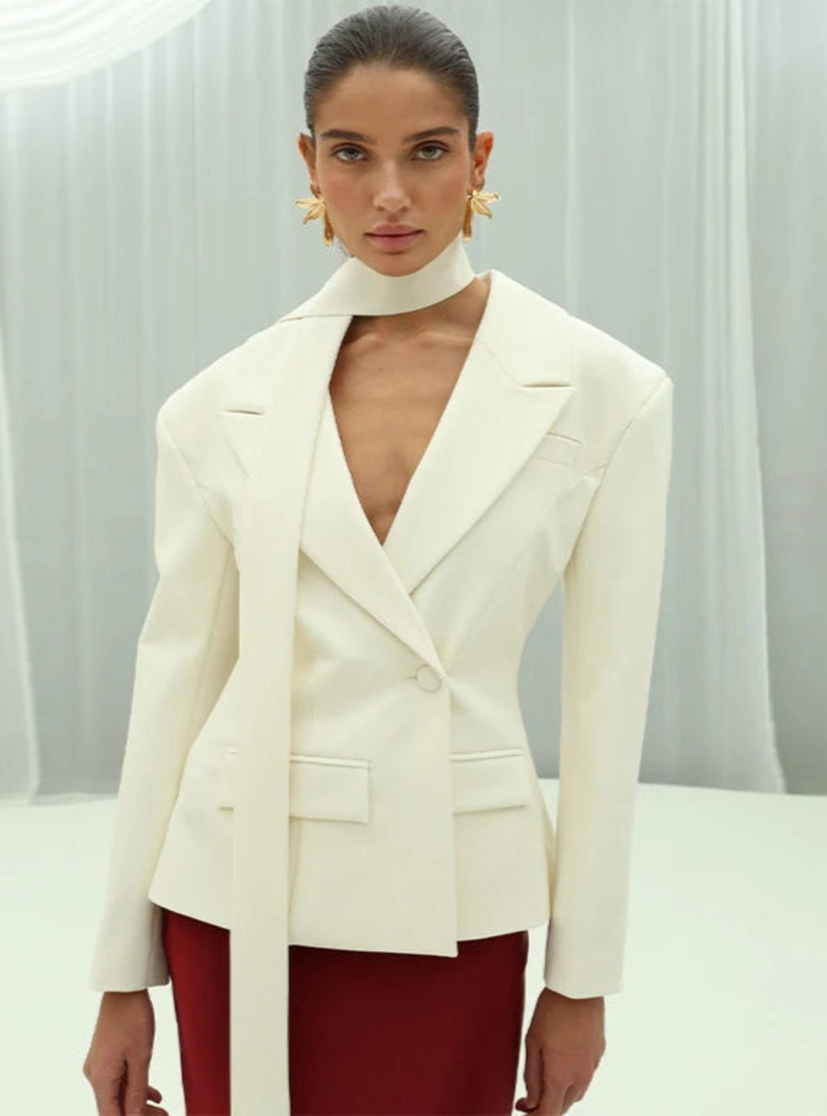 Woman wearing a white blazer over a red outfit with a neutral background