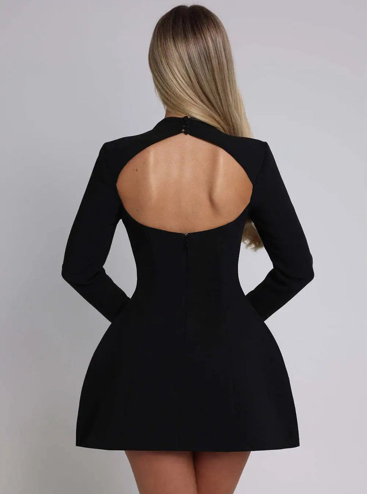 Black dress with open back worn by a model on a plain background