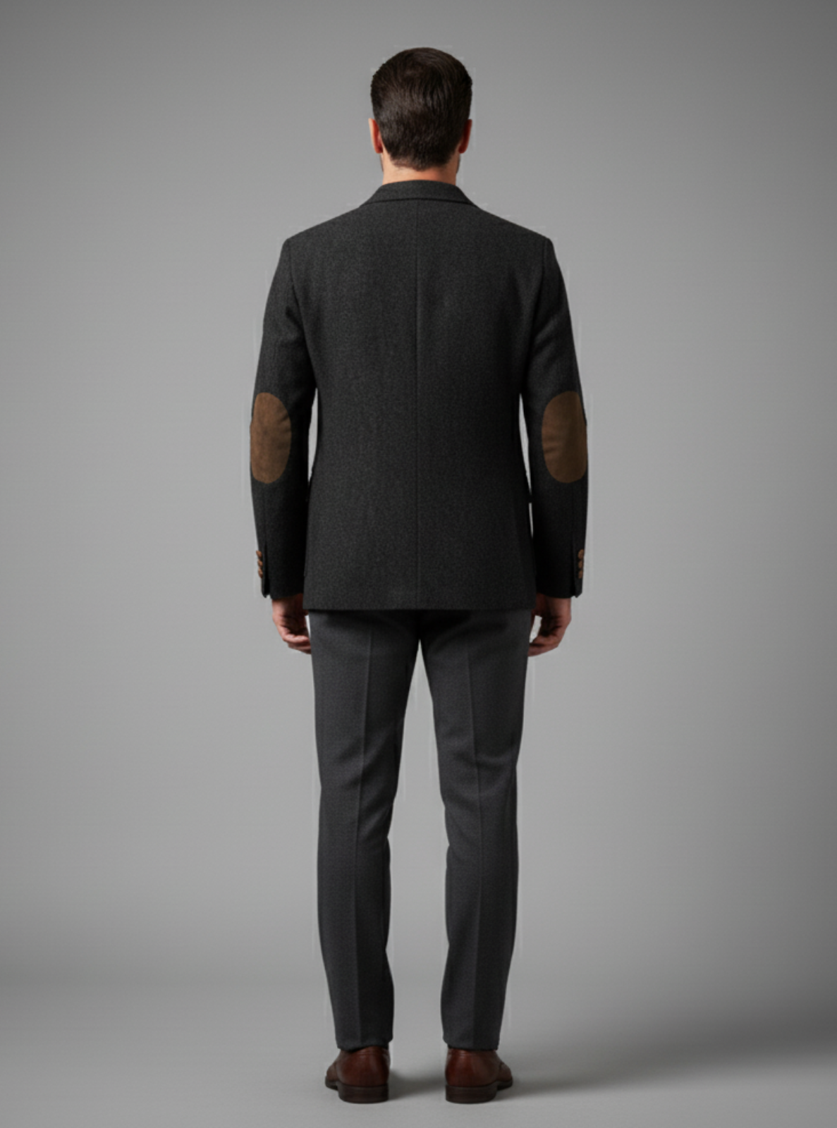 Man wearing a dark gray suit with elbow patches on a gray background