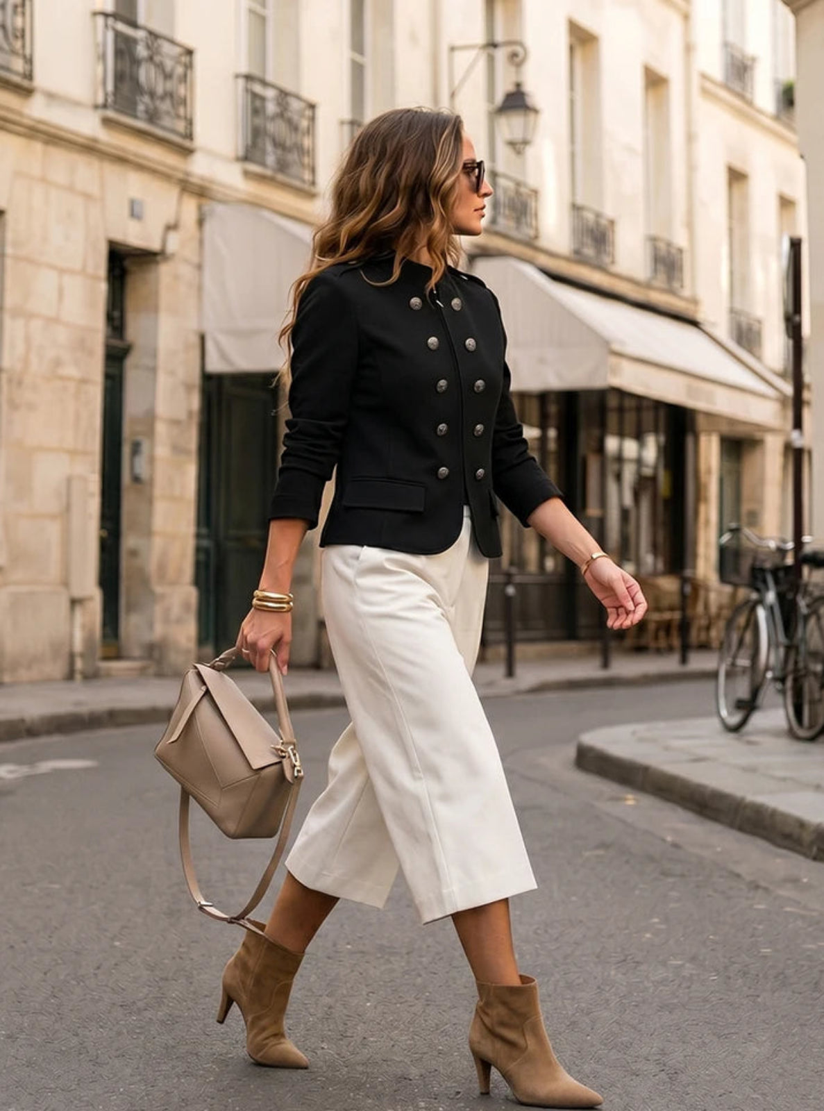 Woman walking on a city street wearing a black jacket, white pants, and brown boots.