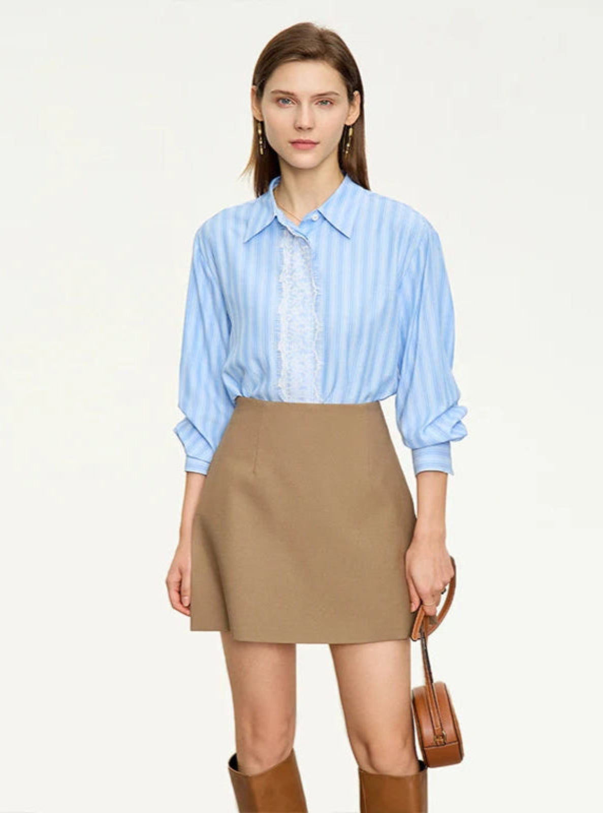 Woman wearing a light blue striped shirt, beige skirt, and brown boots on a white background
