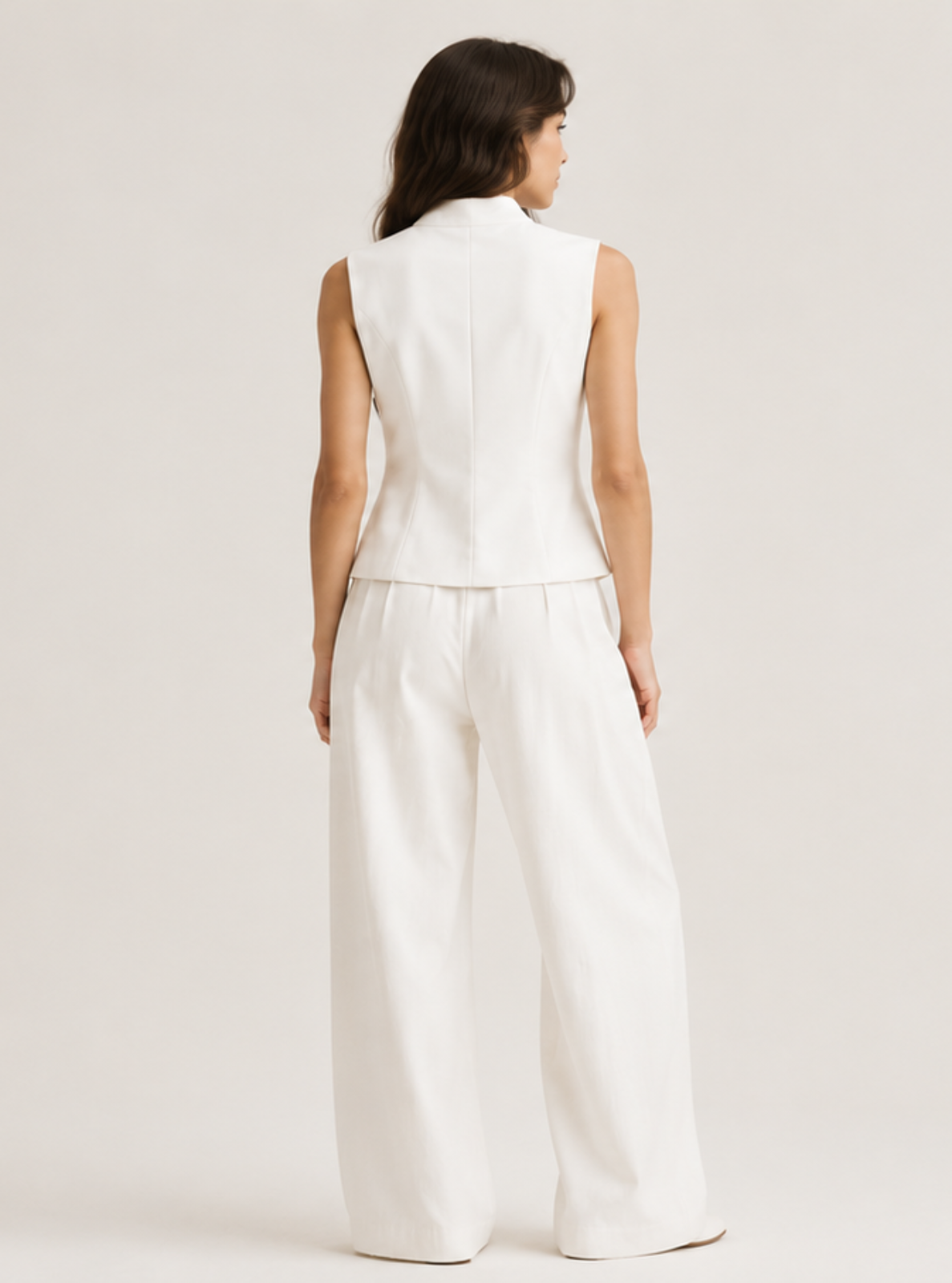 A woman viewed from behind wearing a white sleeveless vest and matching wide-leg trousers against a plain light gray studio background.