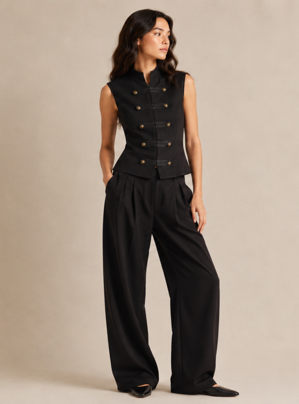 A woman modeling a black sleeveless double-breasted vest with matching wide-leg trousers, standing against a plain beige studio backdrop.
