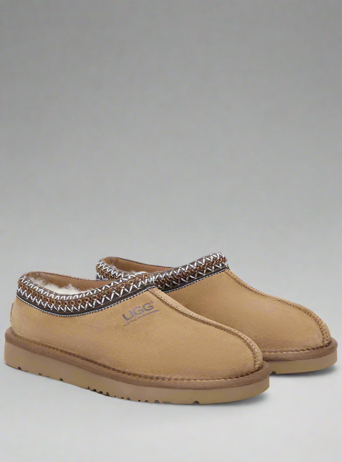 Pair of tan slippers with patterned trim on a gray background