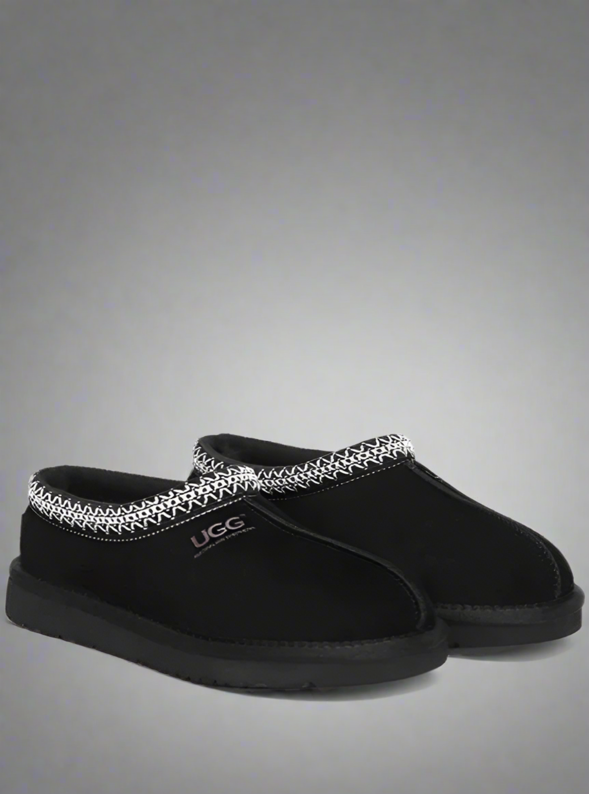 Black UGG slippers with decorative trim on a gray background