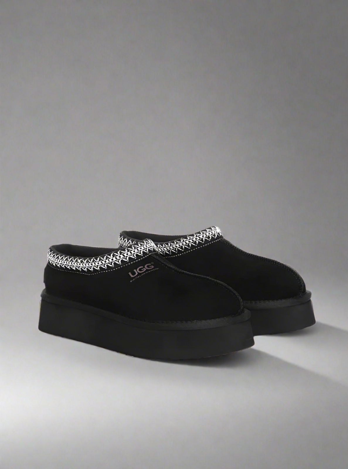 Black UGG slippers with decorative chain on a gray background