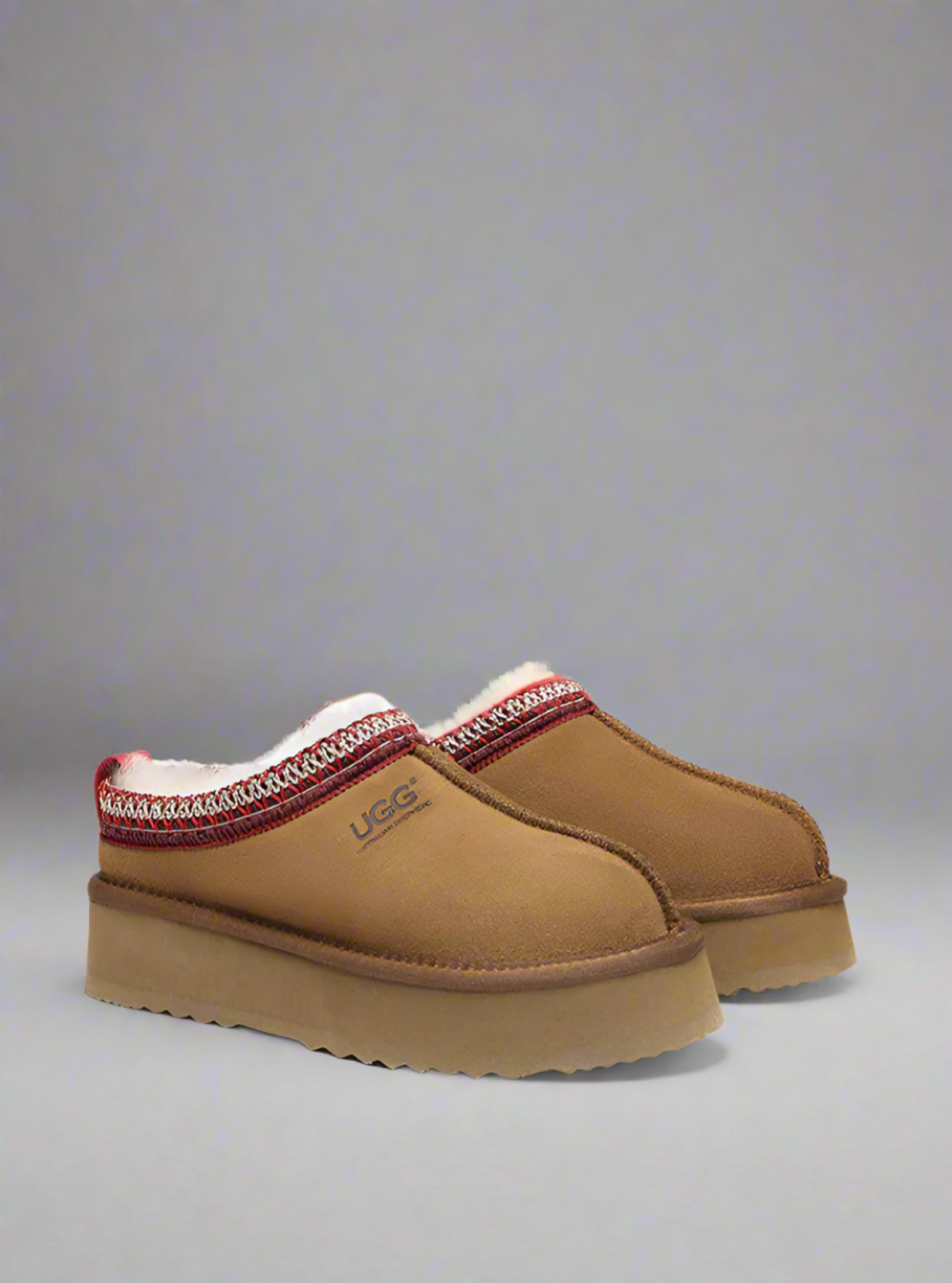 Brown UGG slippers with red and white trim on a gray background