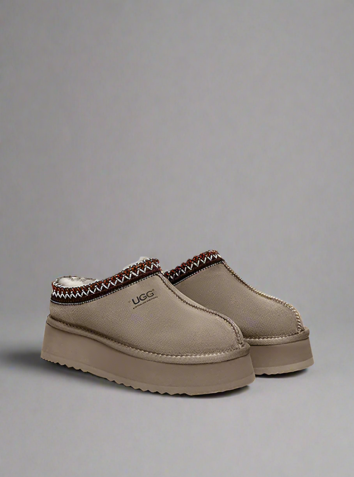 Pair of beige UGG slippers on a white background