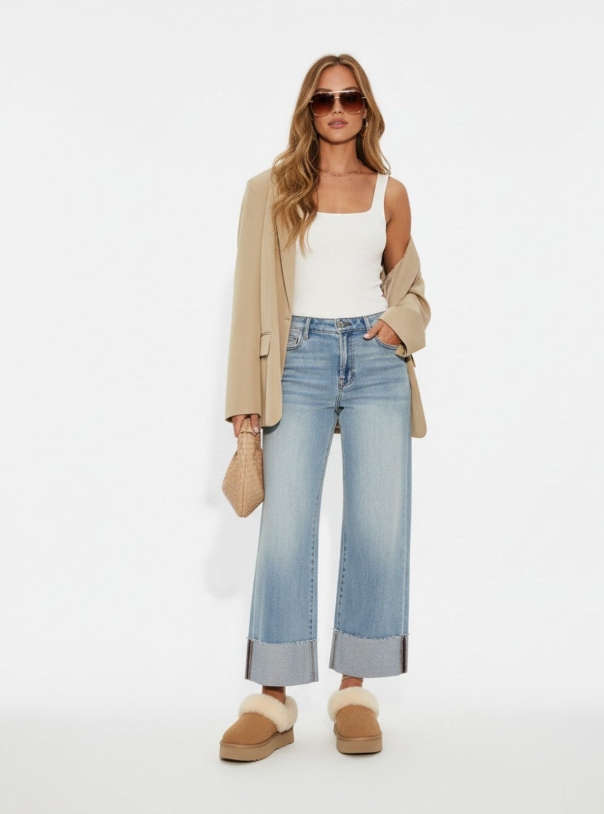 Woman wearing a beige blazer, white top, light blue jeans, and brown shoes on a white background