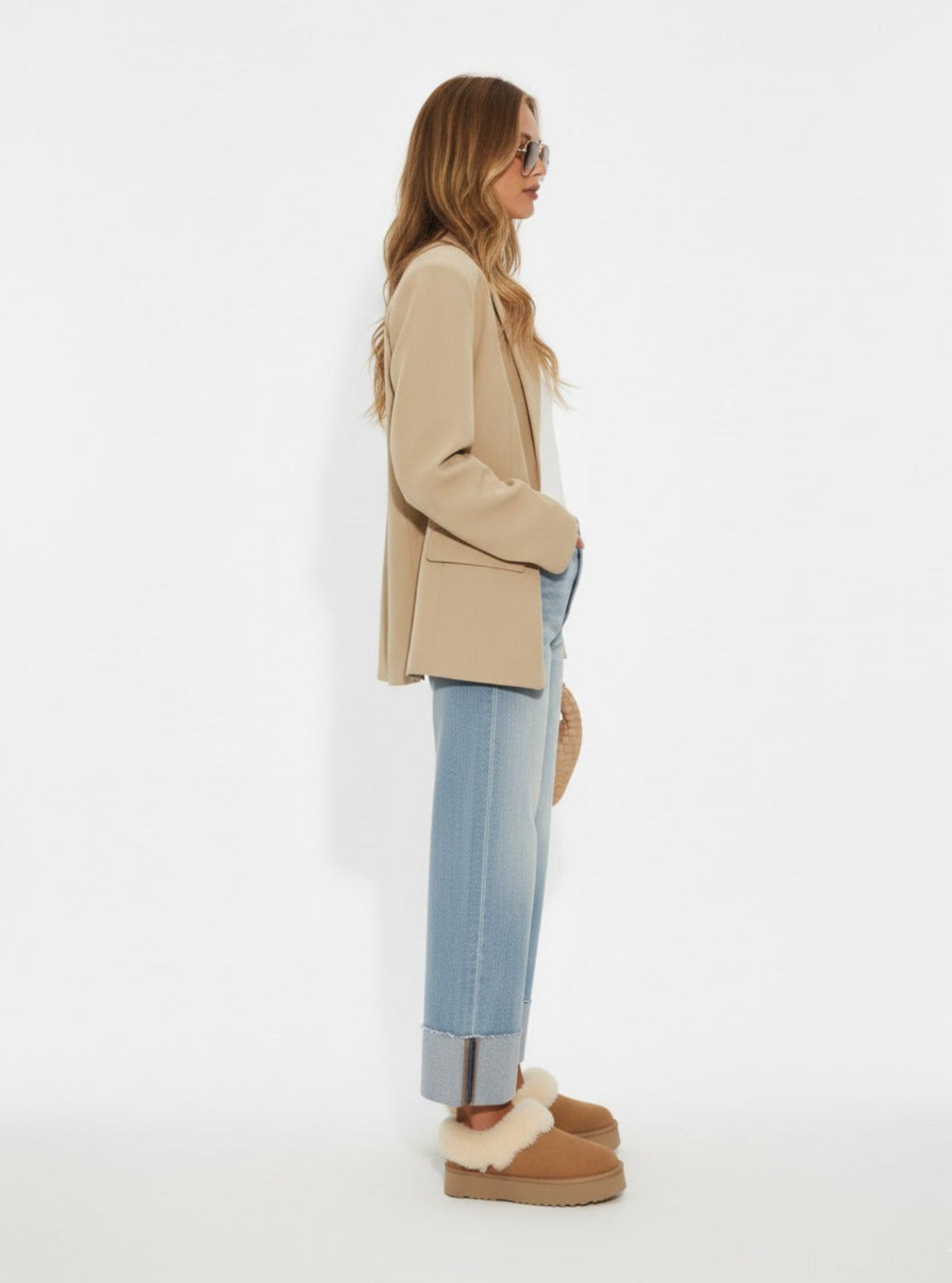 Woman wearing a beige blazer, light blue jeans, and brown shoes on a white background