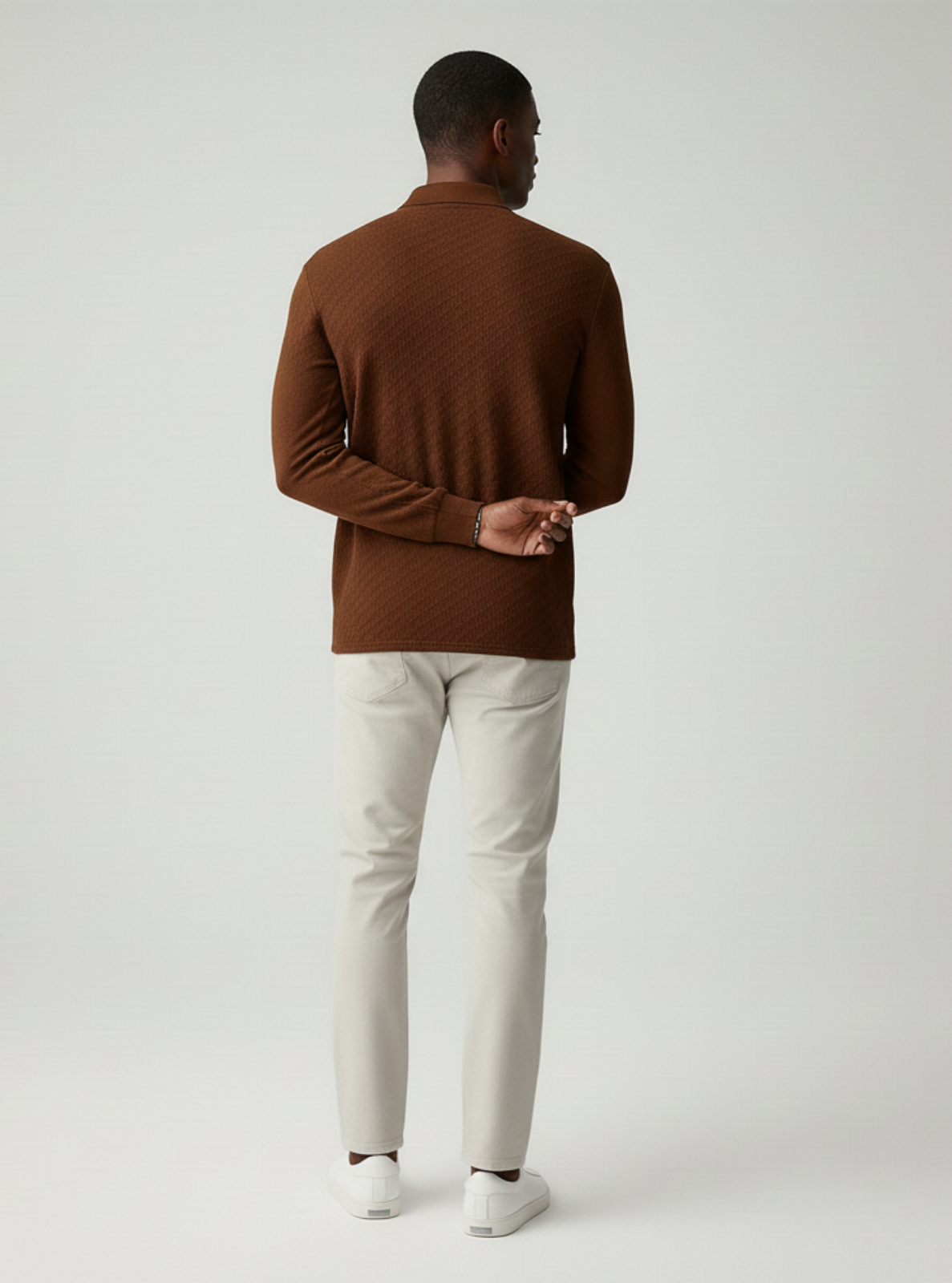 Man wearing a brown sweater and light gray pants on a white background