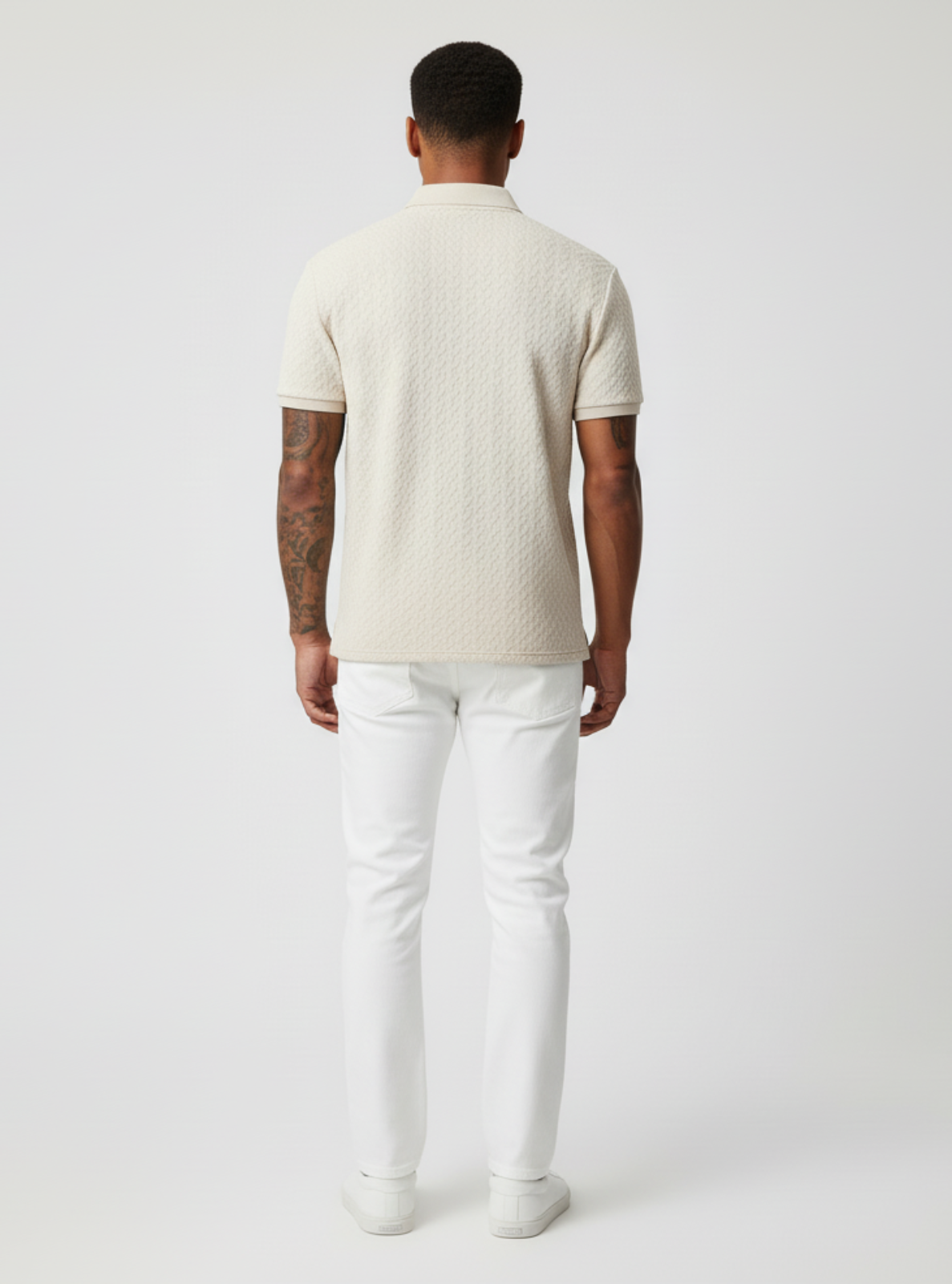 Man wearing a beige sweater and white pants on a plain background