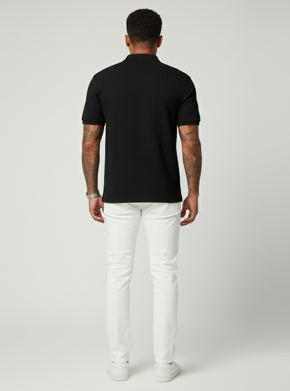 Man wearing a black polo shirt and white pants on a gray background