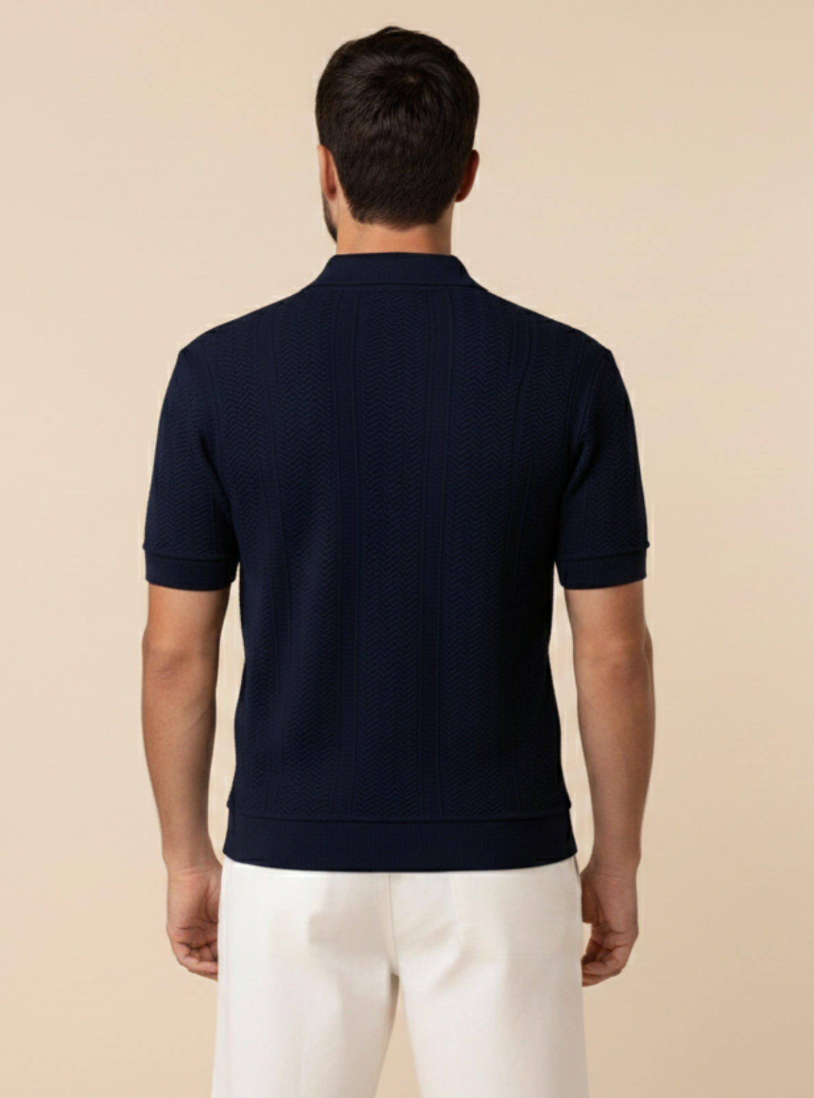 Man wearing a navy polo shirt and white pants on a beige background