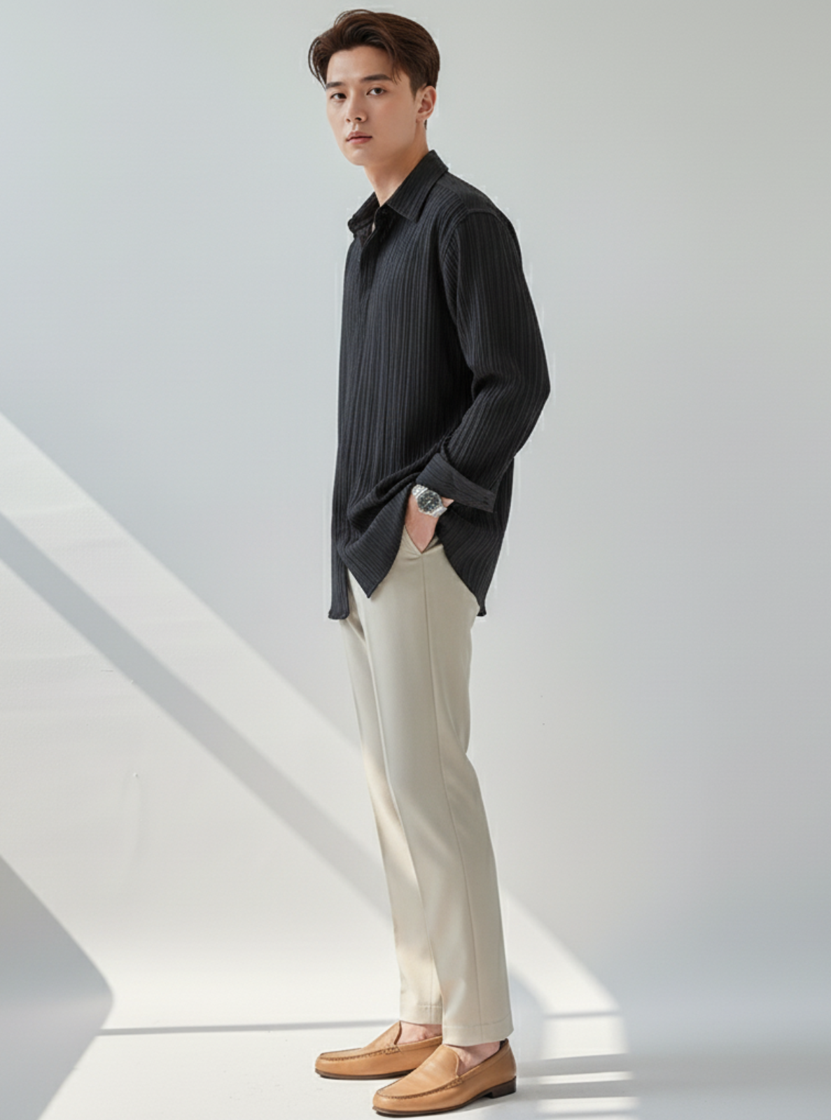 Man wearing a black shirt and beige pants standing against a white background