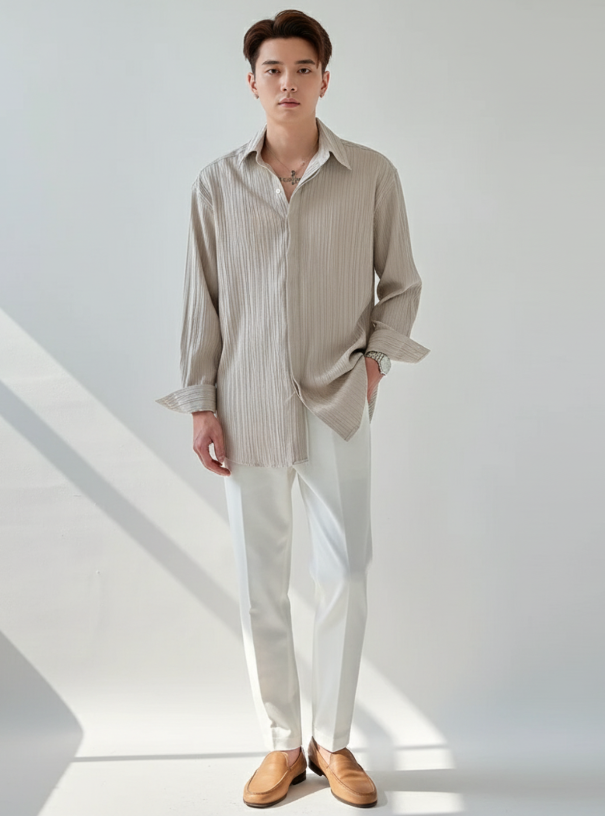 Man wearing a light-colored shirt and pants standing against a white background