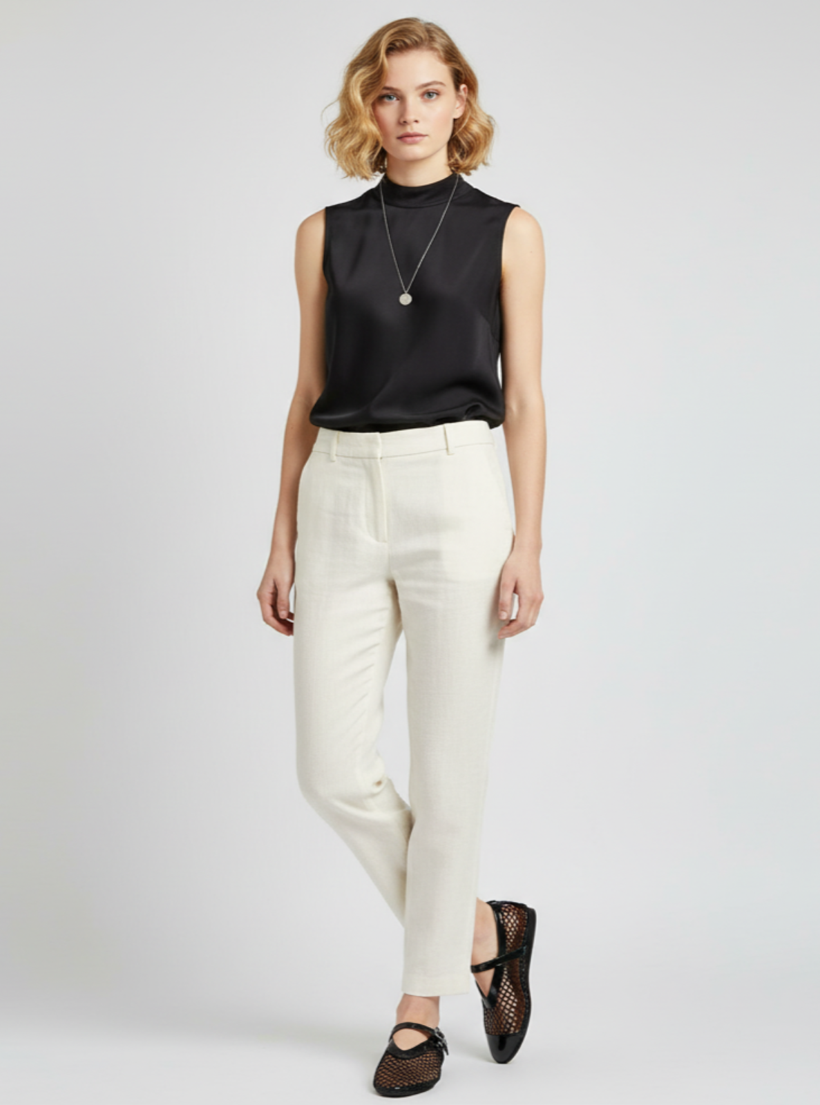 Woman wearing a black sleeveless top and white pants on a light gray background