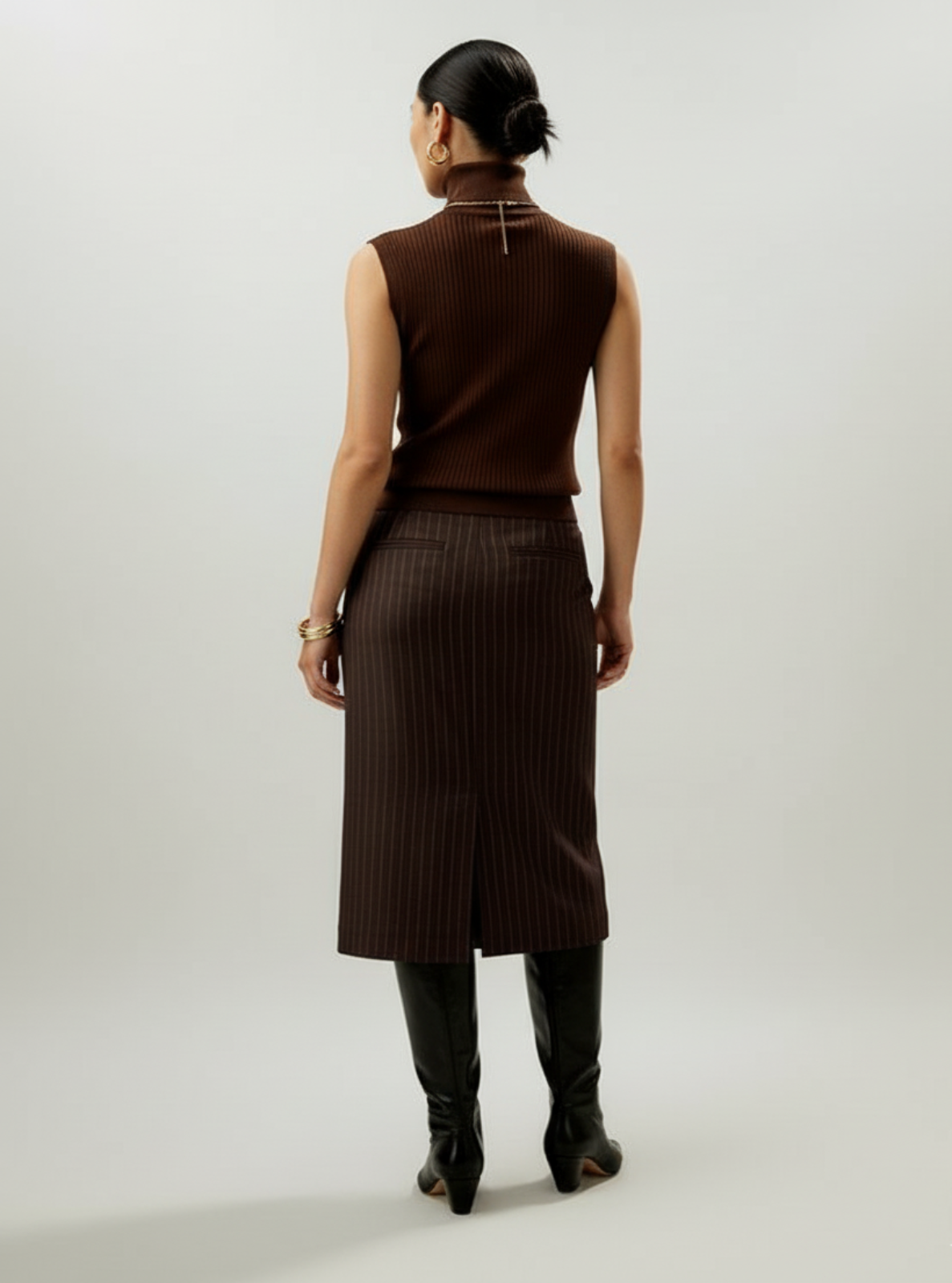 Person wearing a brown sleeveless top and pinstripe skirt on a white background