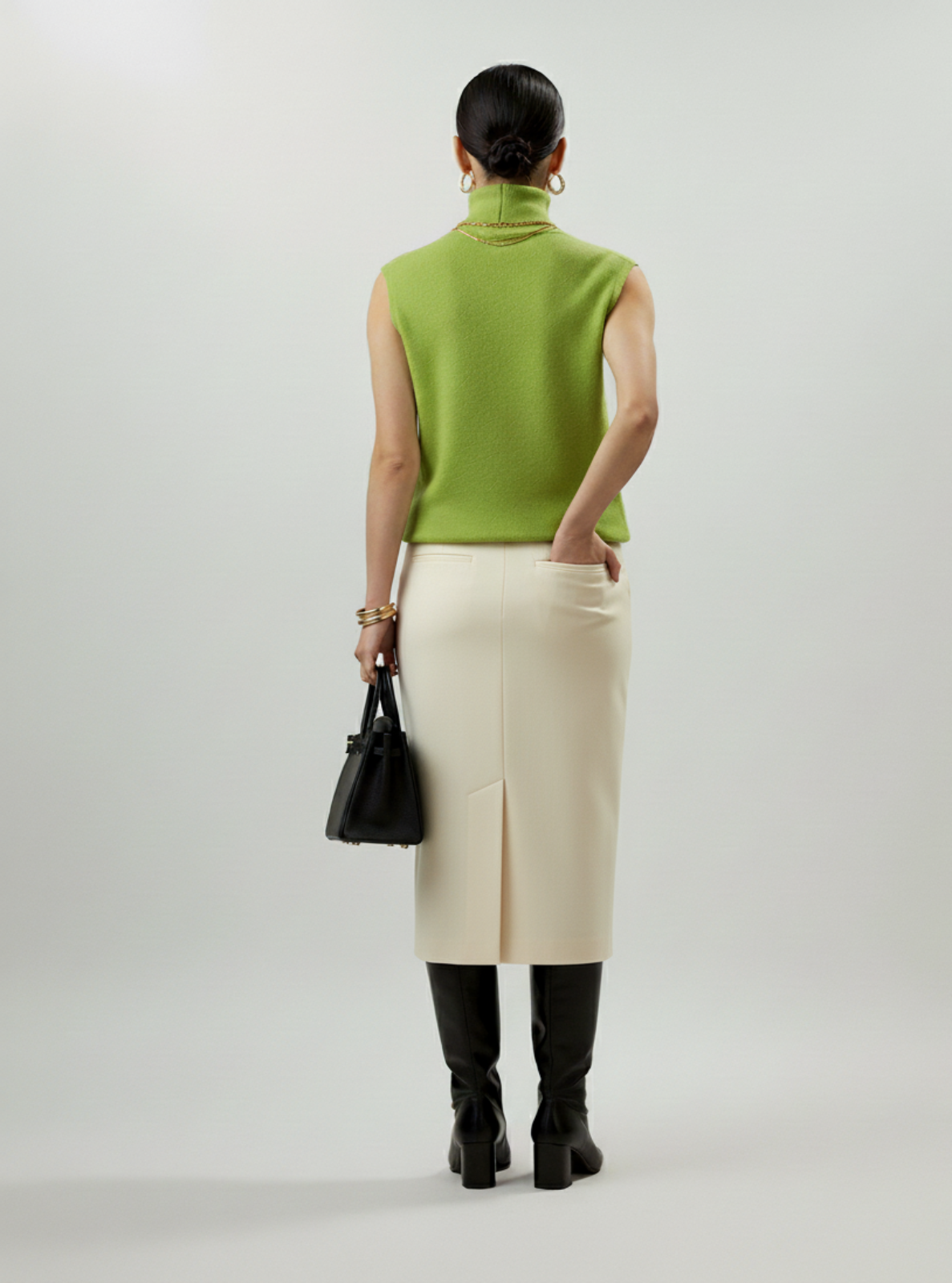 Person wearing a green sleeveless top, white skirt, and black boots on a light gray background