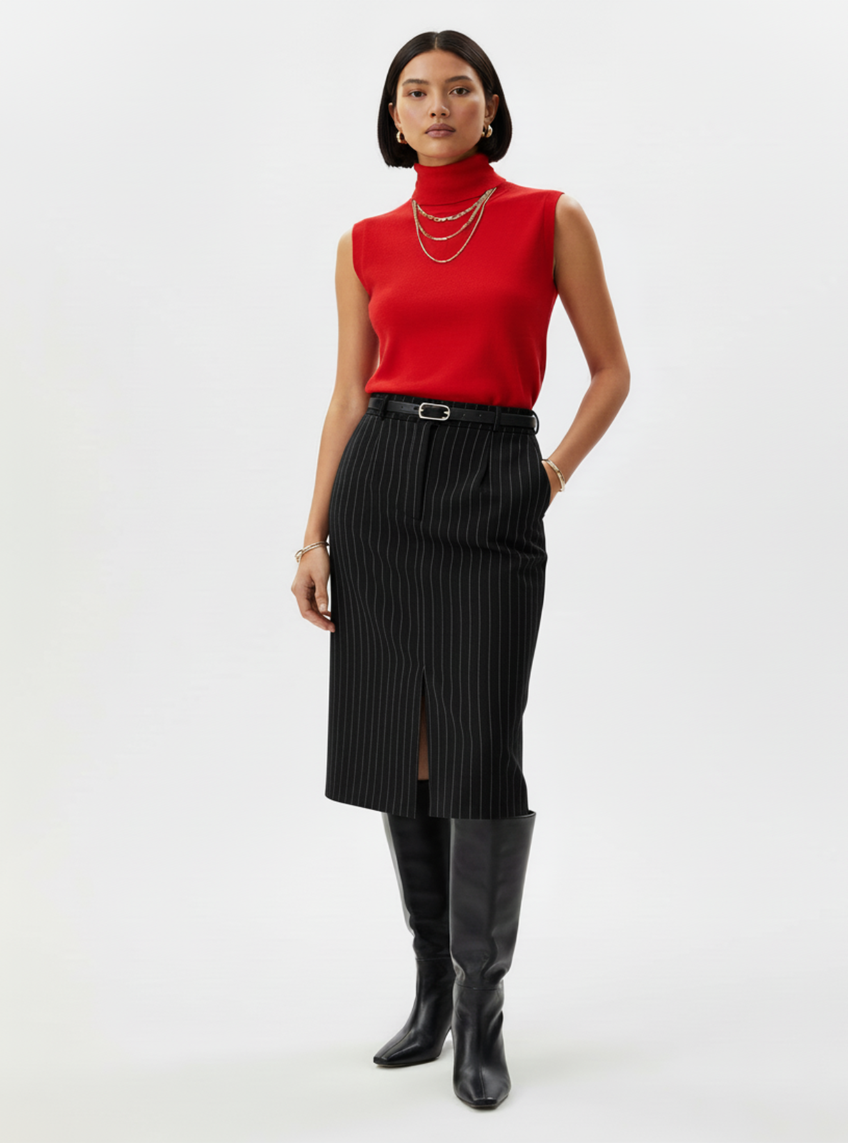 Woman wearing a red sleeveless top, black pleated skirt, and black knee-high boots on a white background